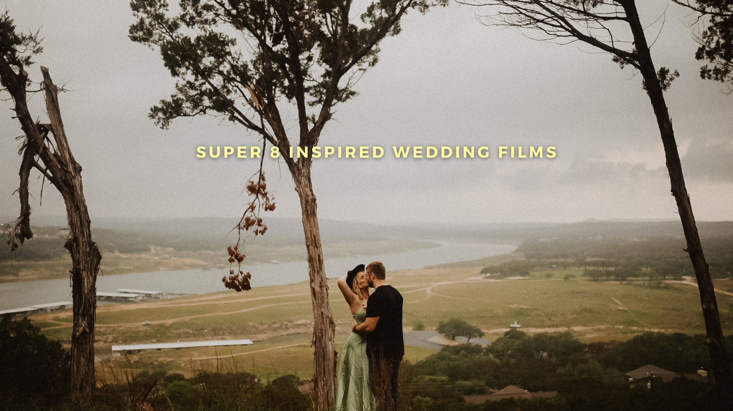A couple embraces on a hilltop overlooking a scenic coastal landscape during a sunset wedding photoshoot.