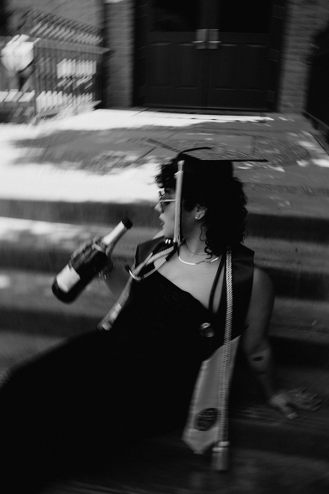 Black and white photo of a woman in graduation cap and gown holding a diploma outdoors.