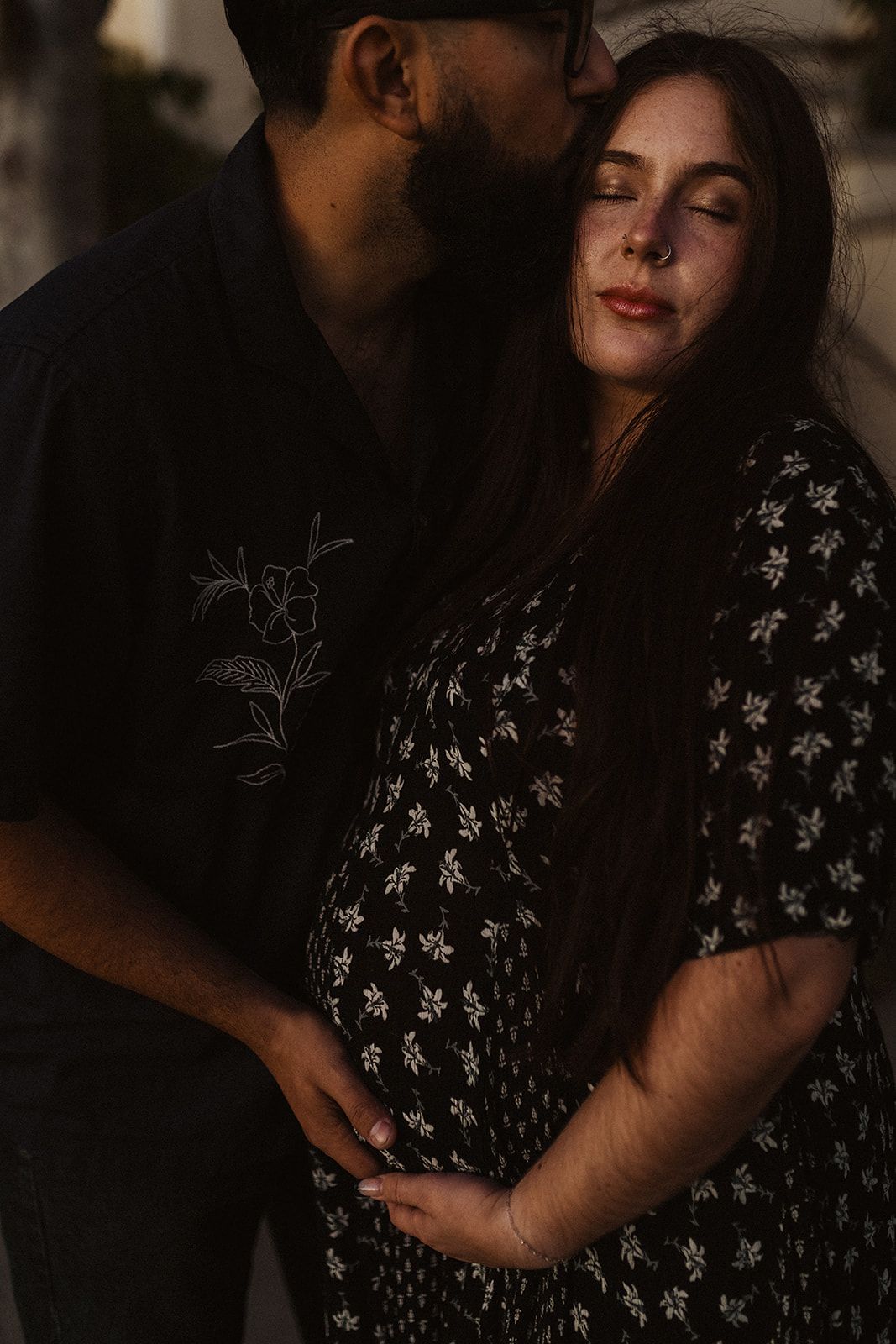 Intimate couple embracing in dark moody lighting while wearing a floral patterned dress.