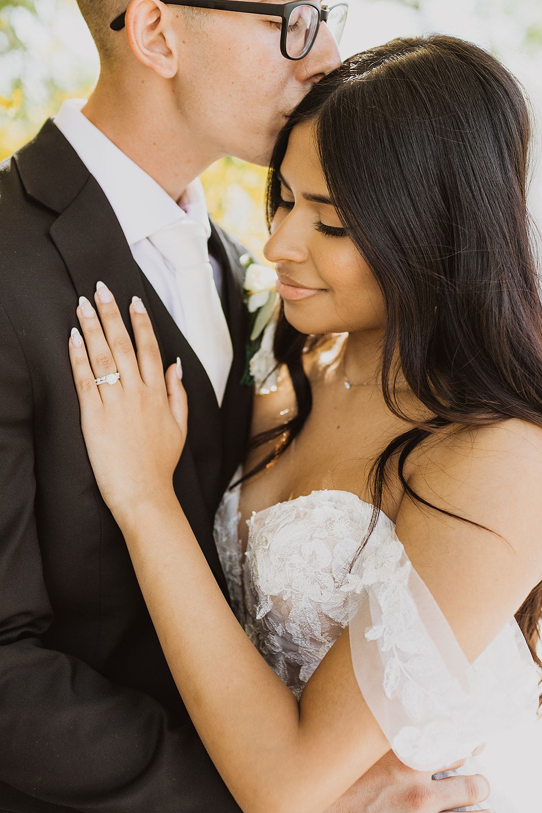 A tender moment between newlyweds showing a close embrace and sparkling engagement ring against a light background.