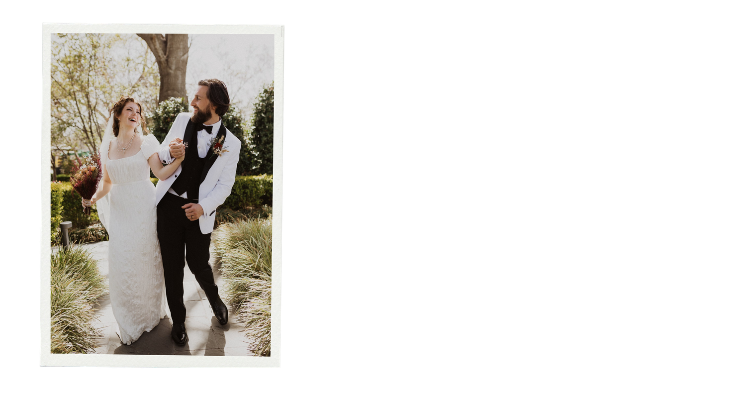 A couple in wedding attire poses together in a scenic outdoor garden setting.