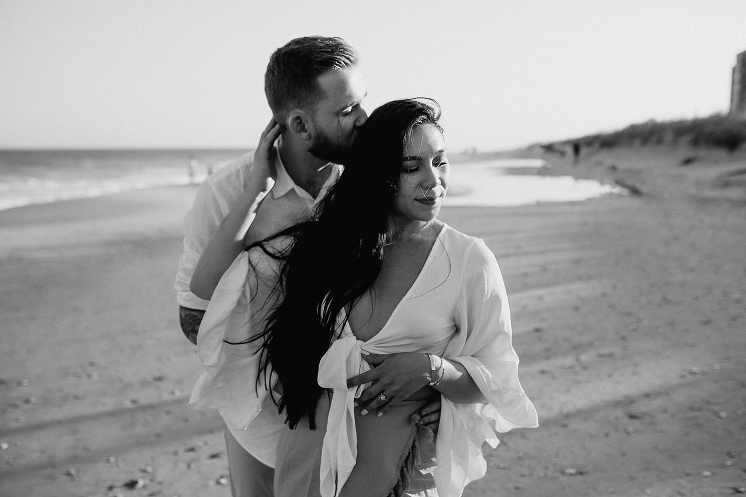 A romantic black and white photo of a couple embracing on a serene beach at sunset.