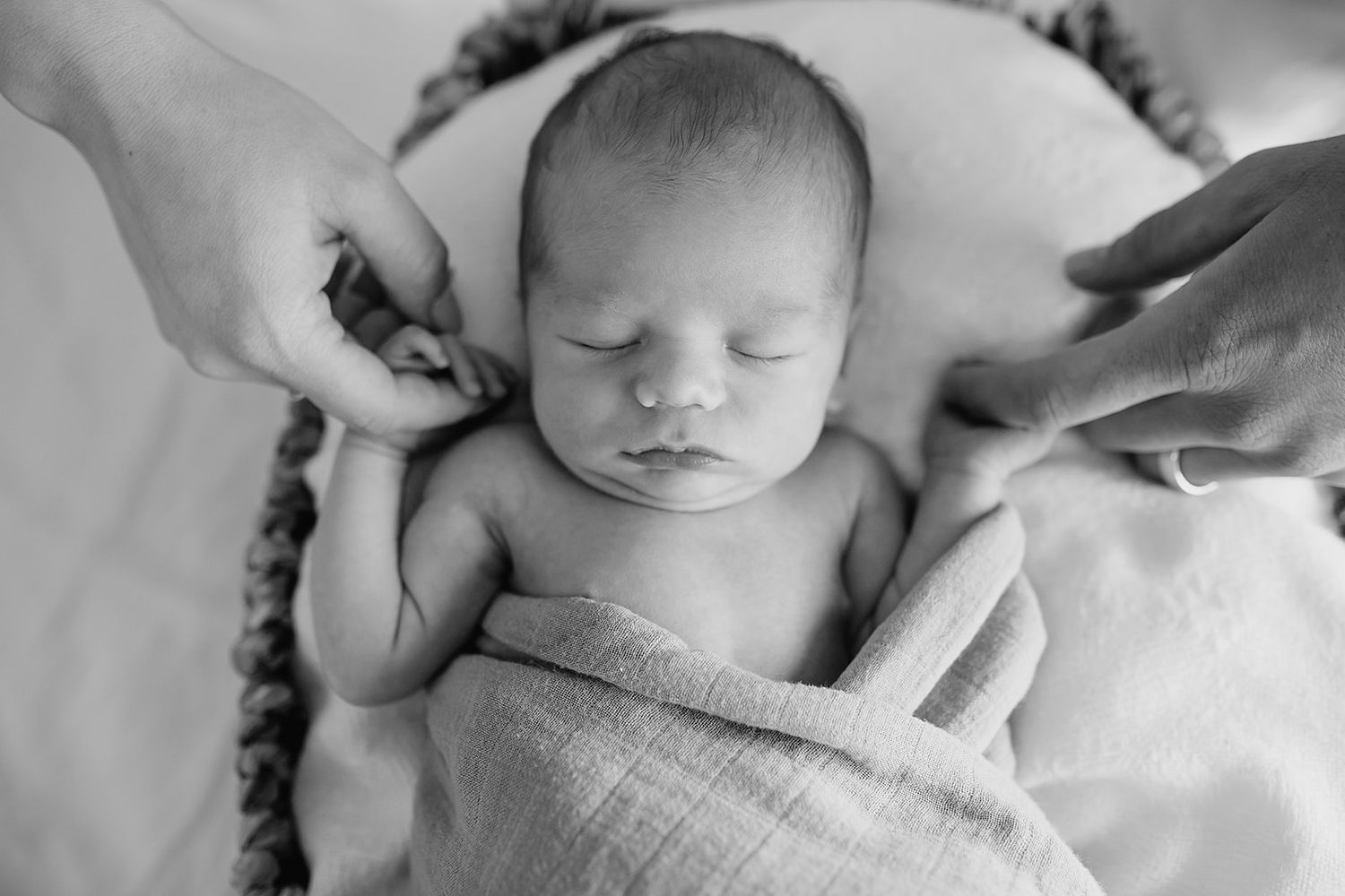 A peaceful sleeping newborn baby wrapped in a soft blanket, captured in black and white photography.