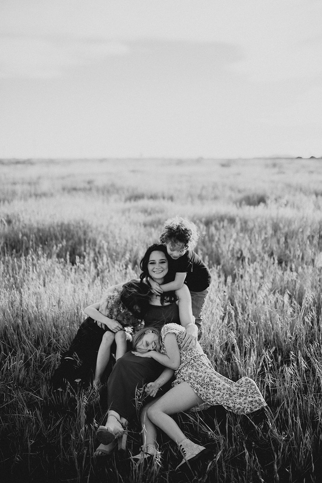 A playful black and white portrait of people embracing and laughing together in a grassy meadow at sunset.