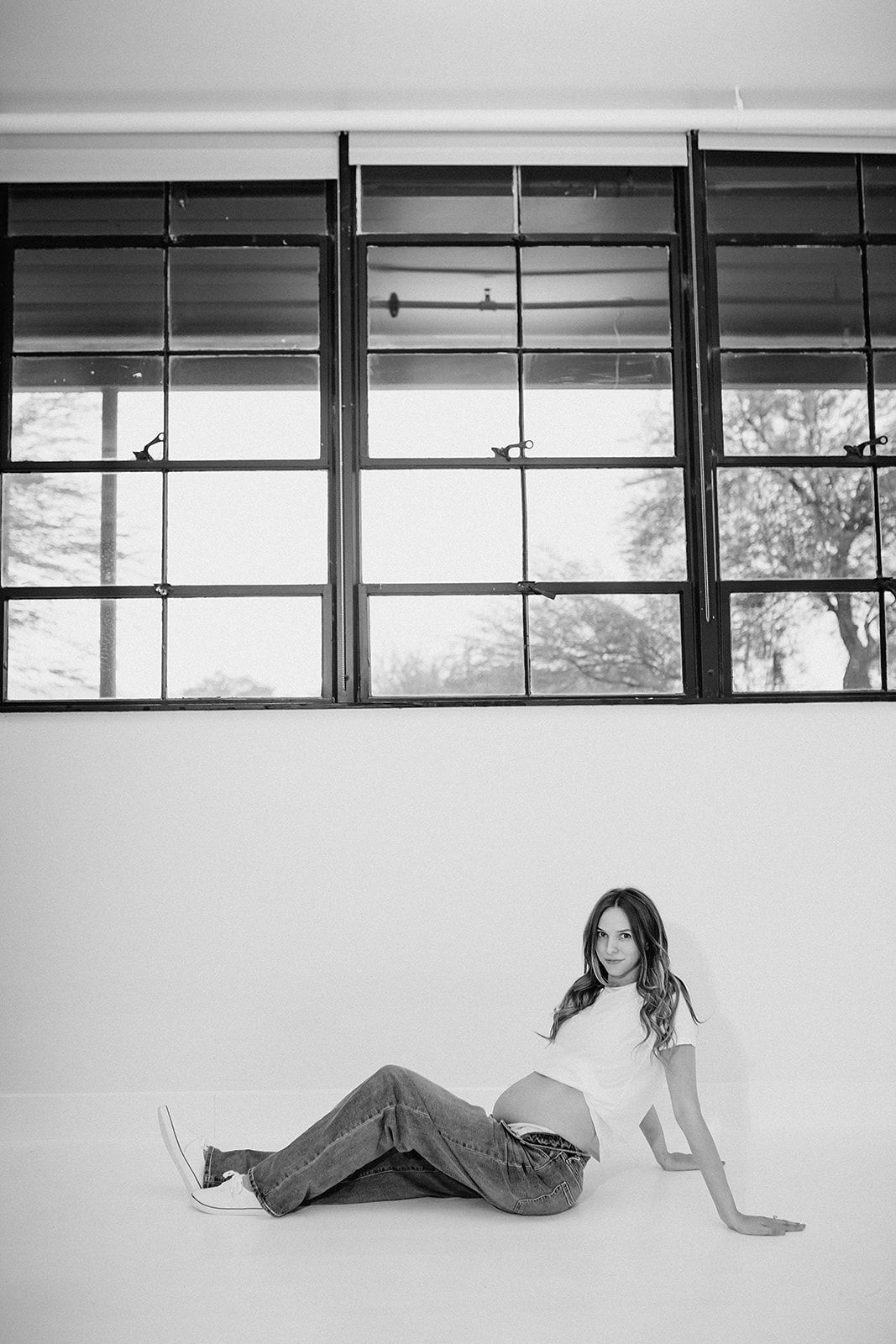 A sequence of black and white photos showing a person lying down and rolling across the floor in a minimalist space.