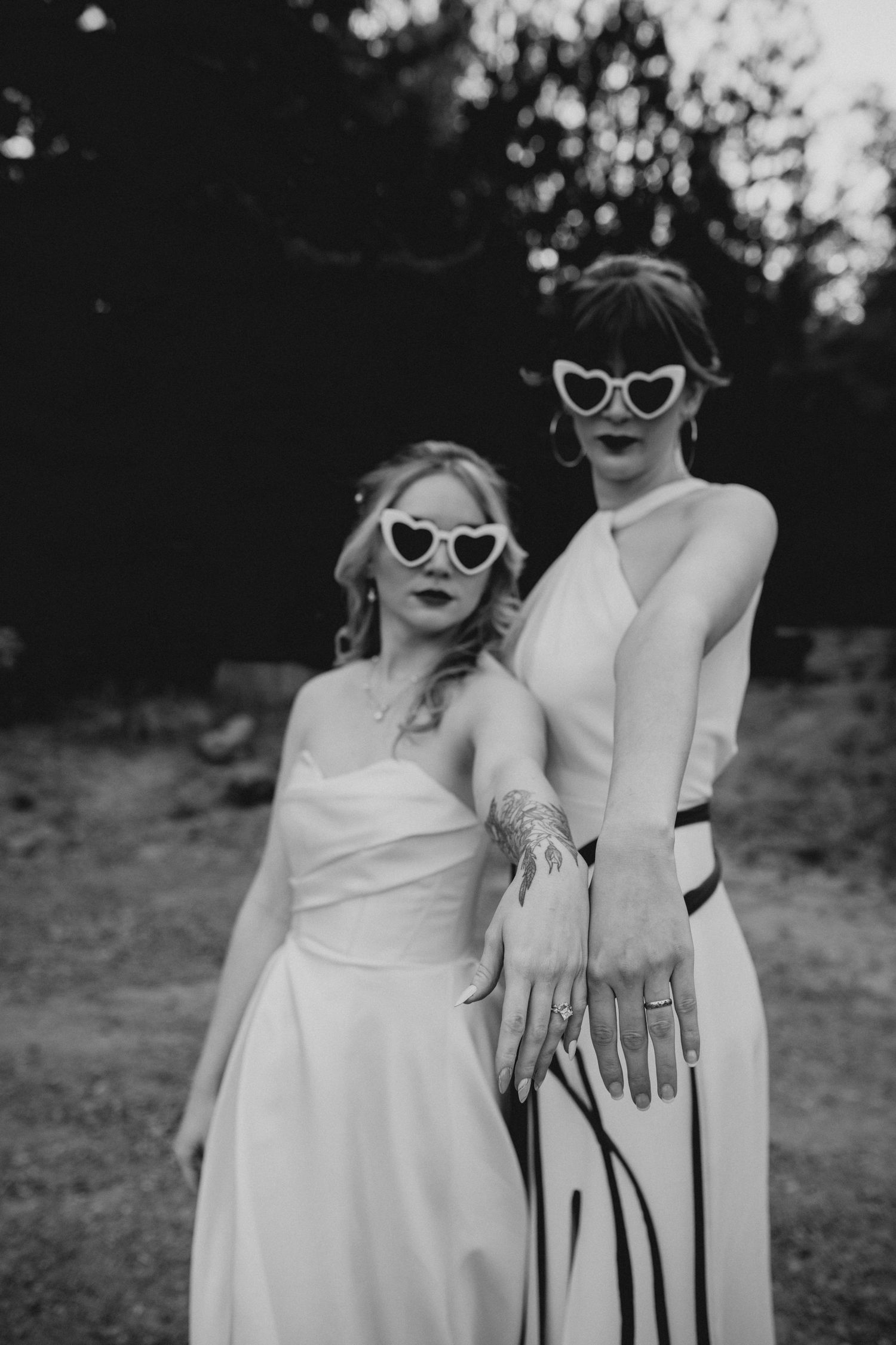 A couple in white outfits and retro sunglasses pose playfully in a series of black and white outdoor photos.