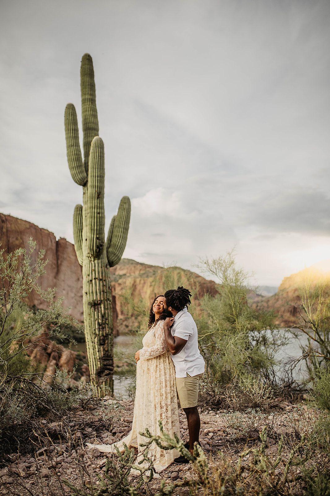 Desert landscape with tall saguaro cactus and rocky terrain under moody cloudy skies at sunset.