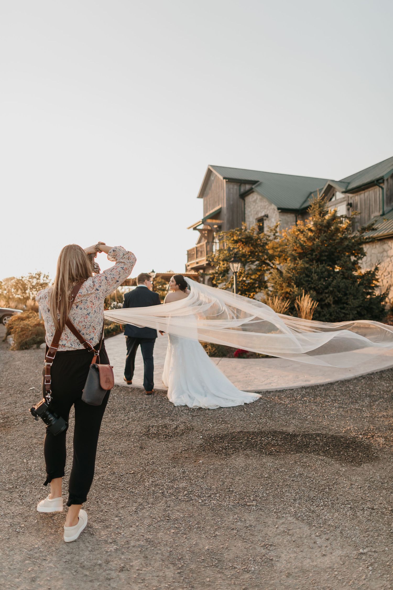 Behind-the-scenes shot of a photographer capturing a bride's flowing veil in the wind.