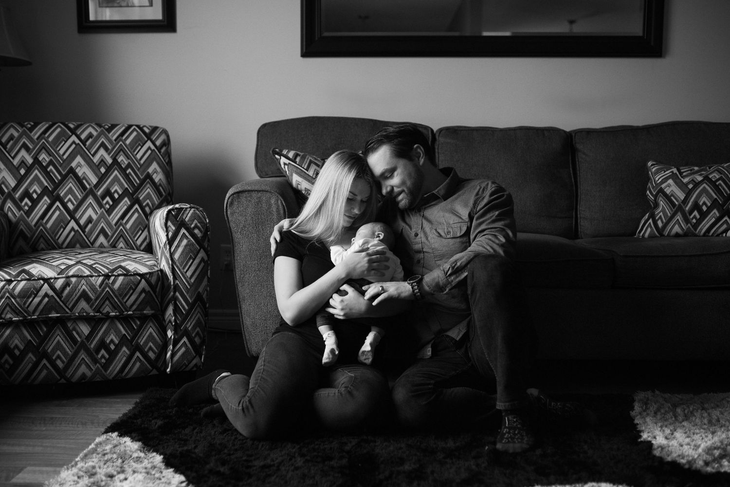 An intimate black and white portrait of a family sharing a quiet moment together on their sofa.