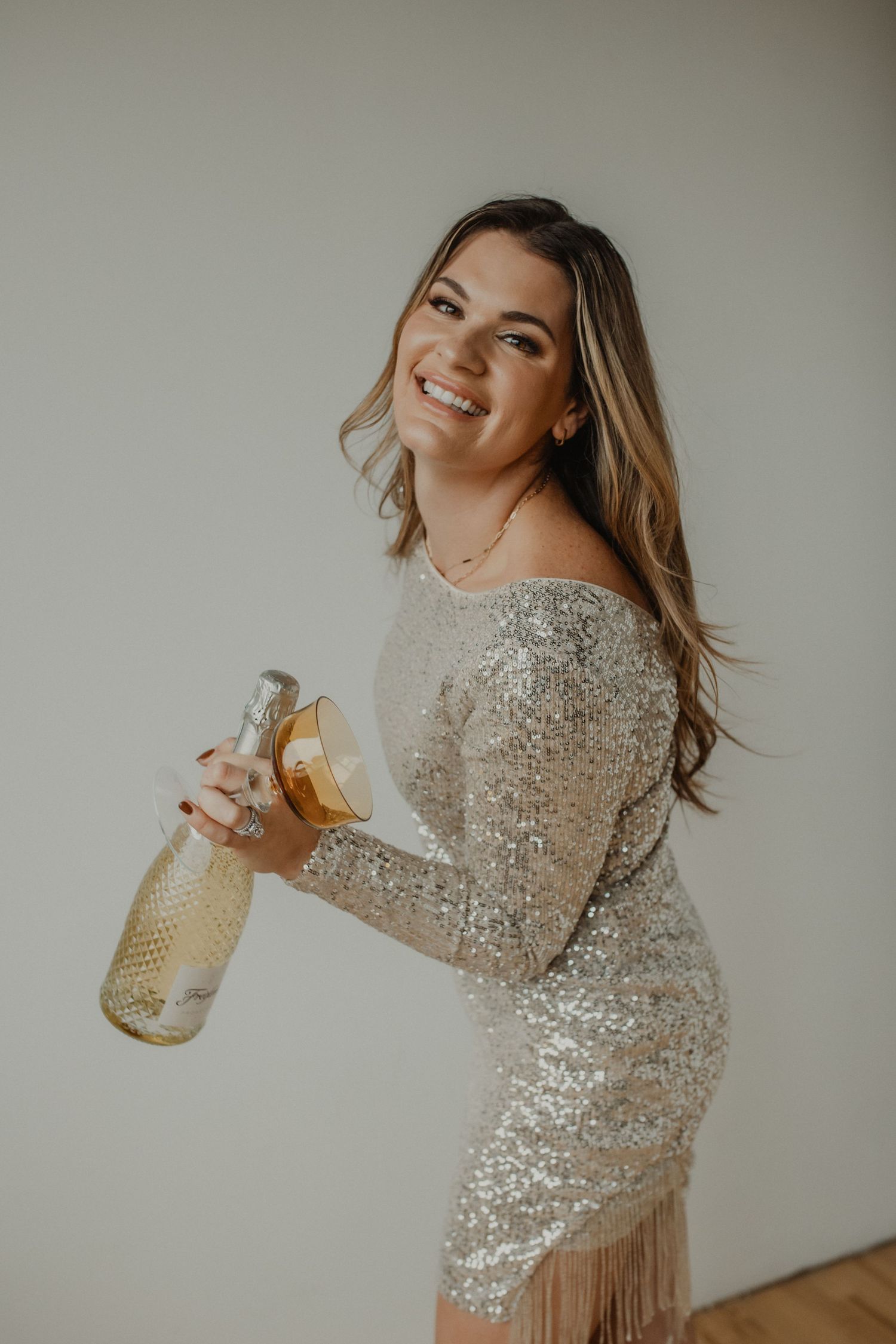 A festive series of shots showing someone in a sparkly silver sequin dress holding and posing with a champagne bottle.