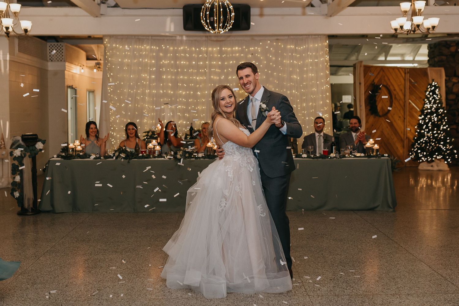 Couple dances in an elegant reception hall with twinkle lights and grey table settings.