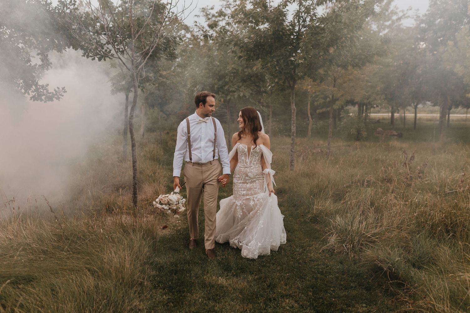 Couple walks through foggy field in rustic wedding attire.