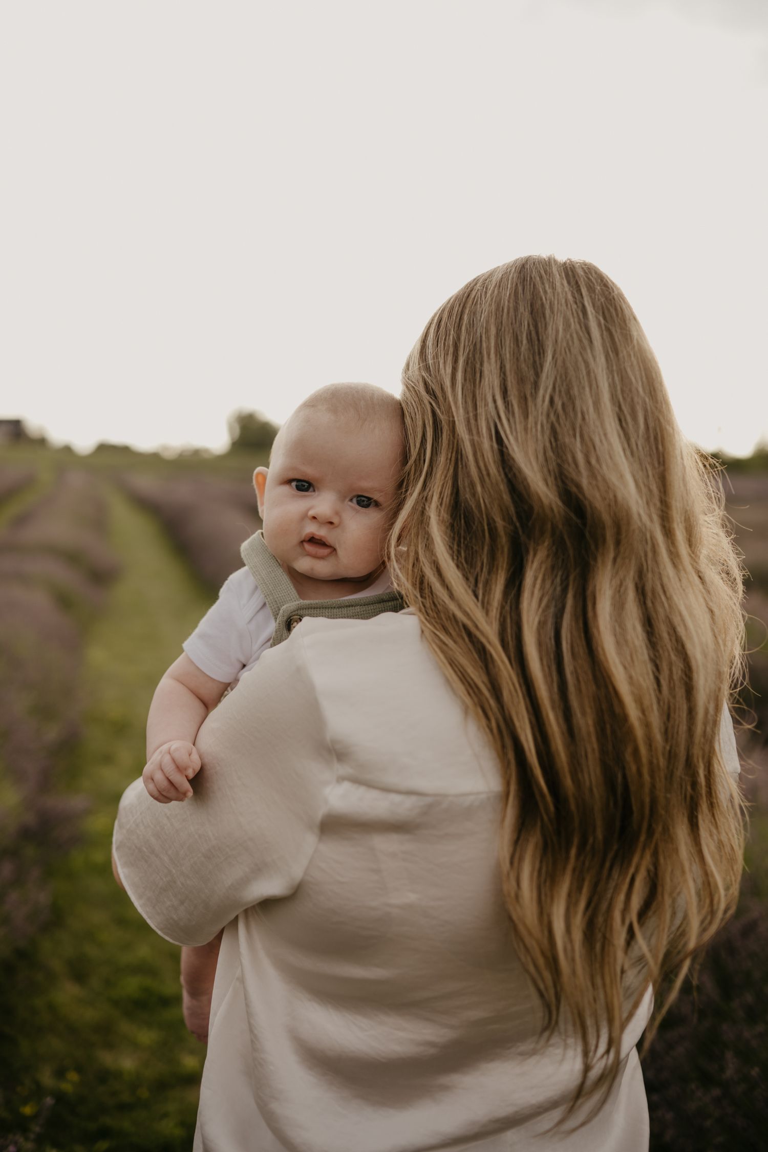 Mother with long blonde hair holding her baby in a lavender field at dusk.