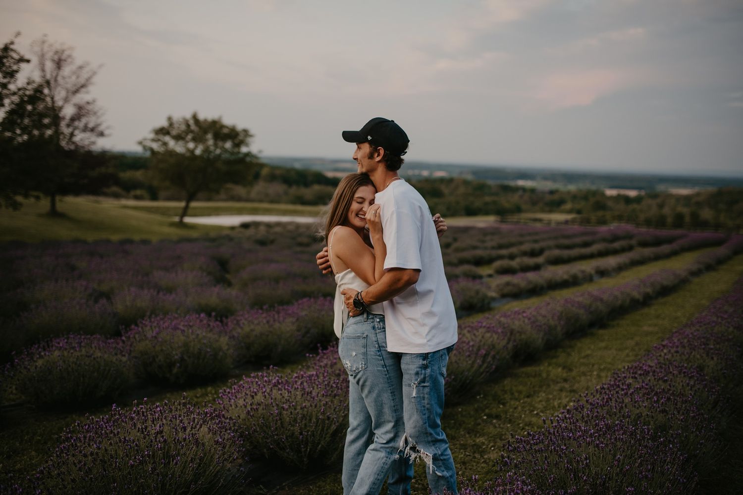 Couple sharing a tender embrace while standing in rows of purple lavender field at sunset.