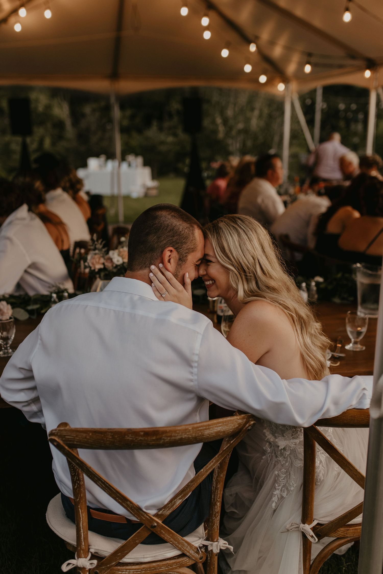 Bride and groom sharing a tender moment at their wedding reception under string lights.