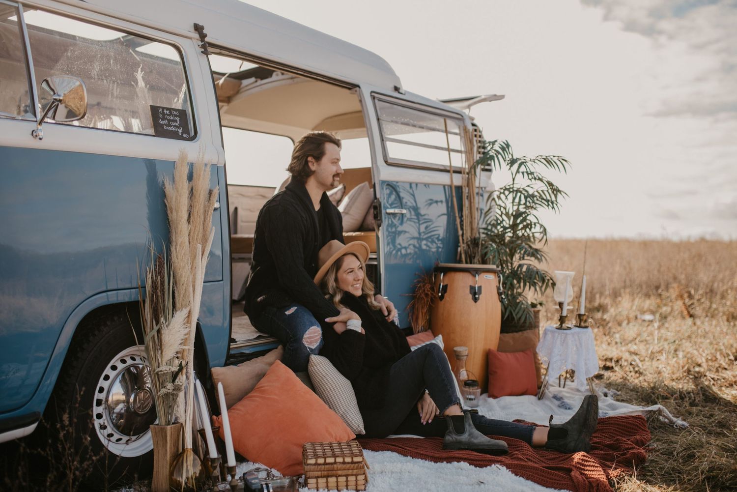 Couple relaxing together beside a vintage blue VW van during a boho-style outdoor engagement session.