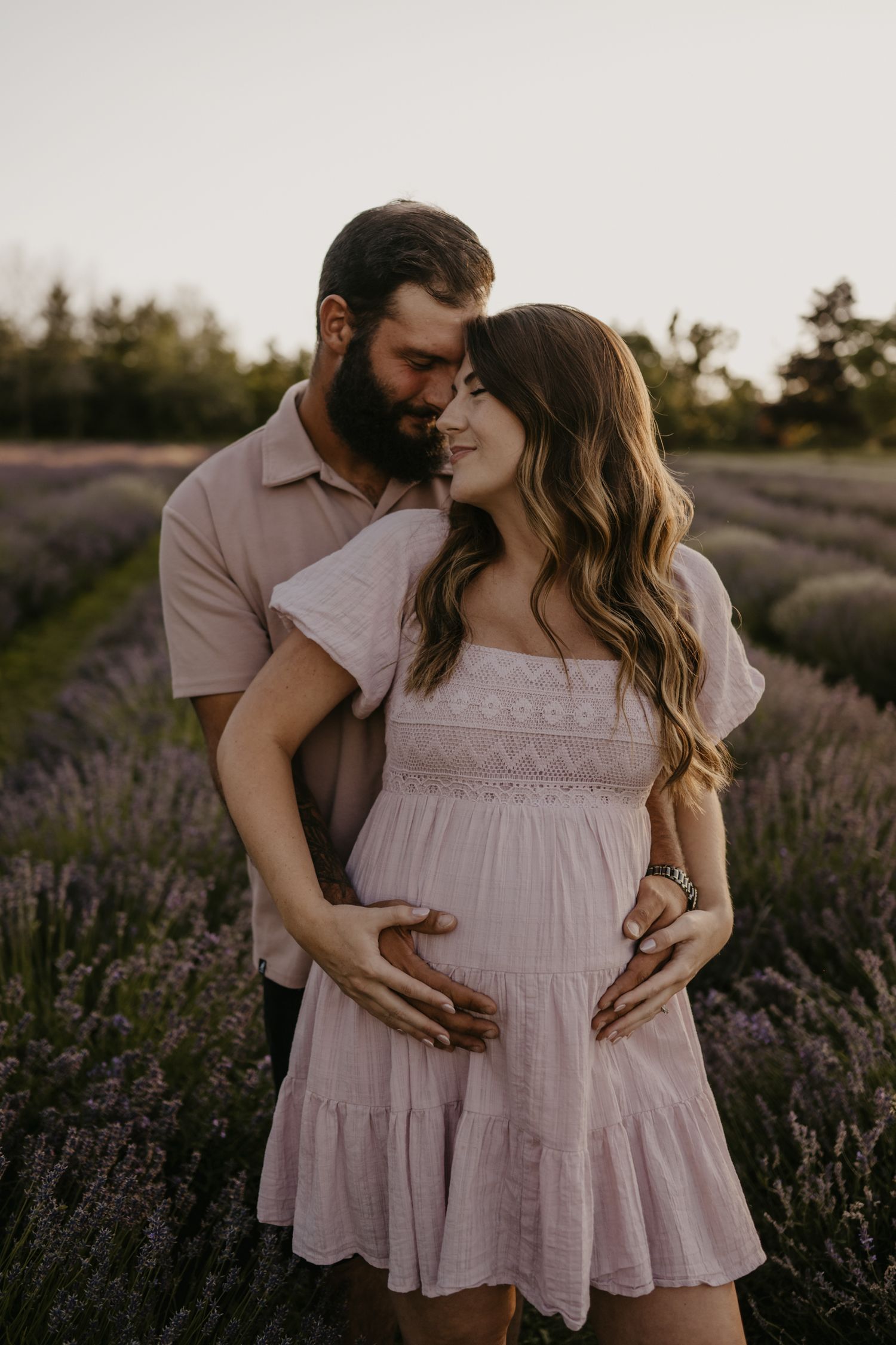 Expecting couple embracing tenderly in a lavender field at golden hour sunset.
