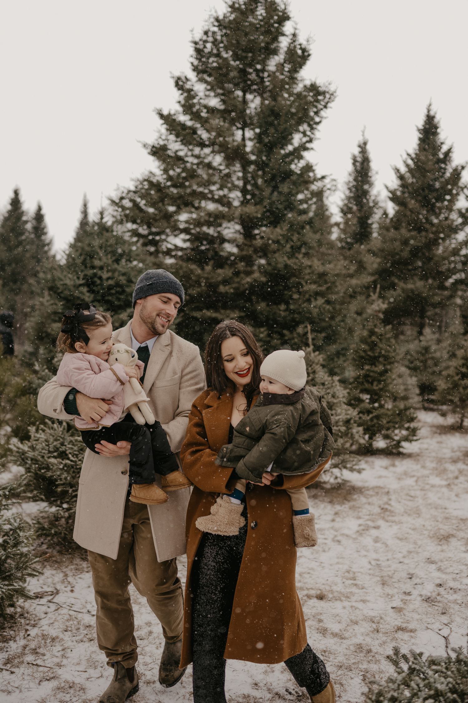 Happy family with two toddlers posing in a snowy Christmas tree farm during winter.