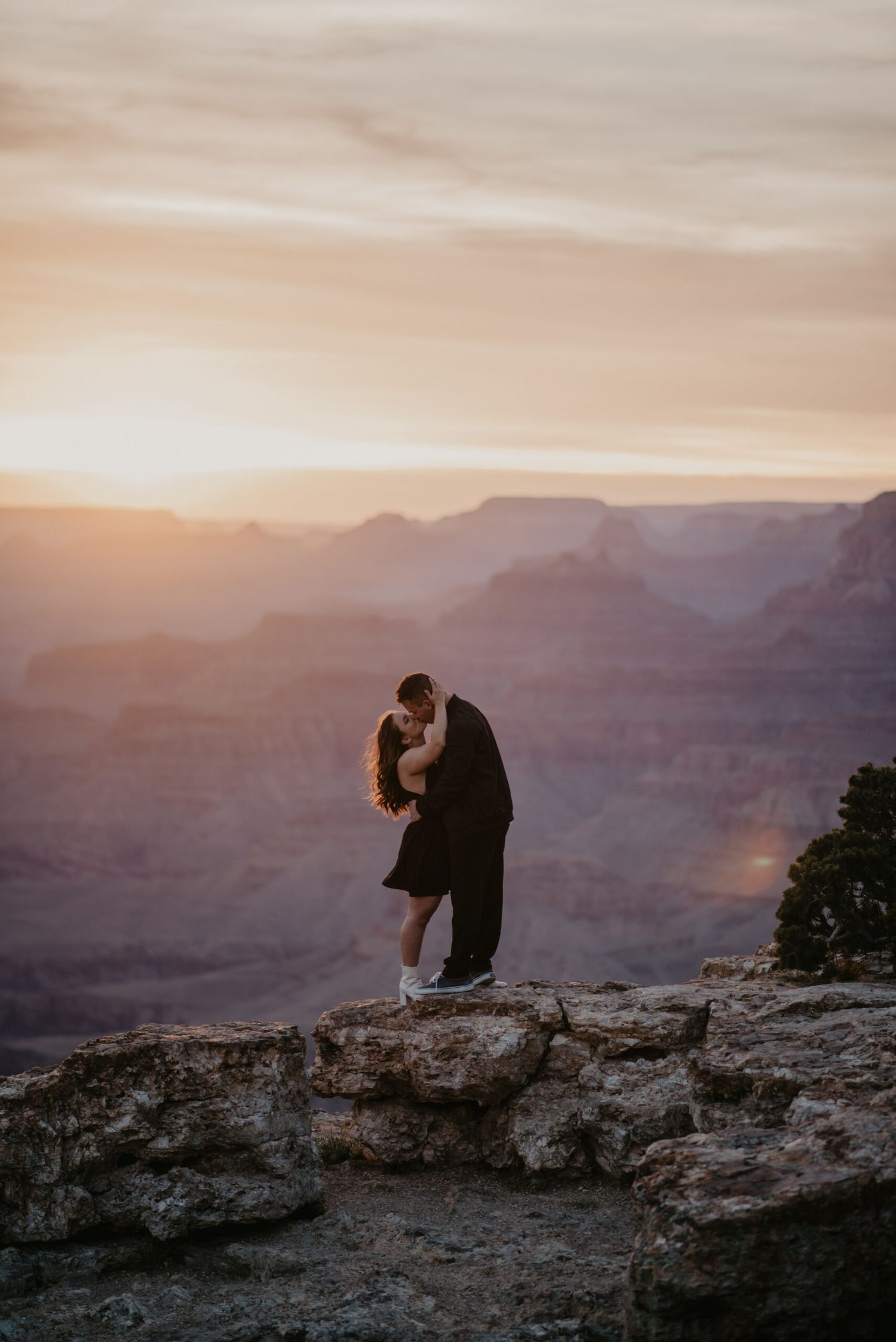 Couple kissing on rocky overlook at Grand Canyon during breathtaking golden sunset.