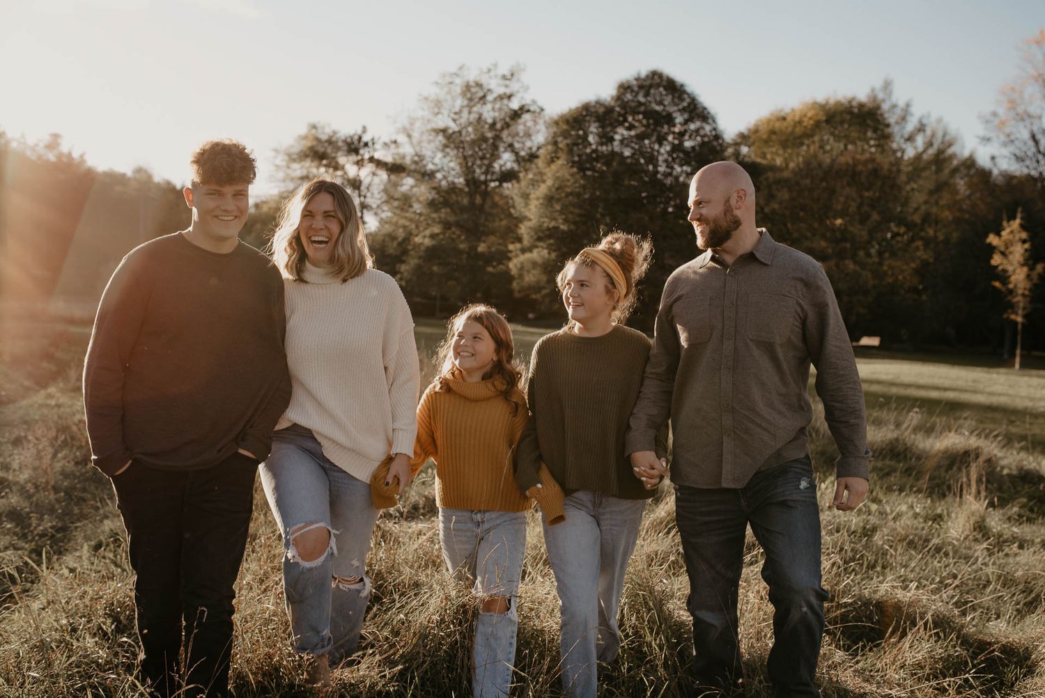 Happy family of five walking together through a sunlit autumn field holding hands.