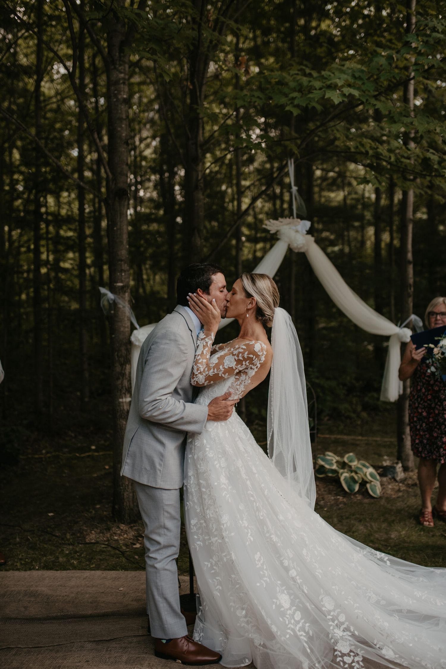 Bride and groom sharing their first kiss at an outdoor woodland wedding ceremony.
