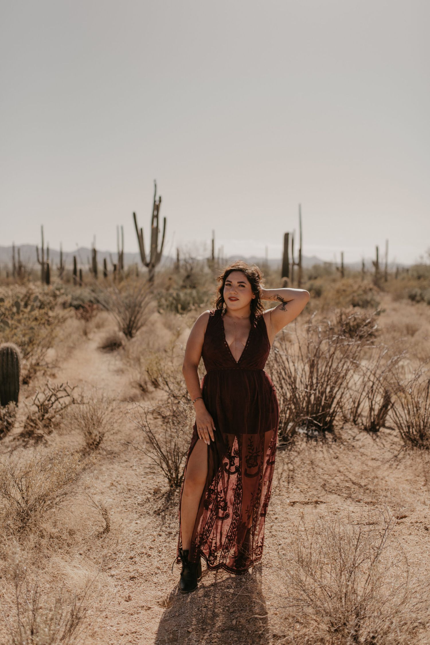 Woman in dark lace maxi dress posing among saguaro cacti in the Arizona desert landscape.