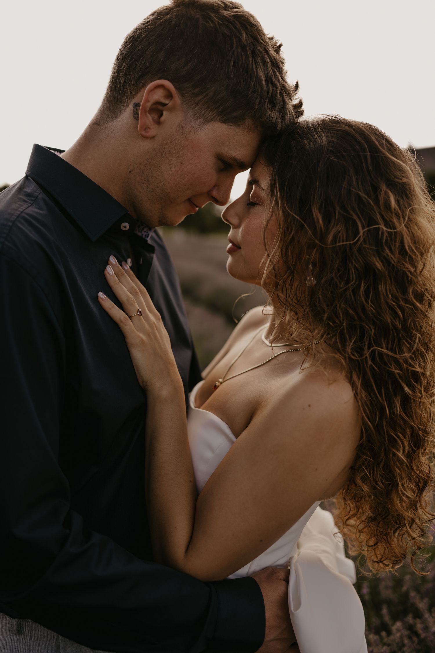 Romantic couple with foreheads touching in an intimate embrace outdoors at dusk.