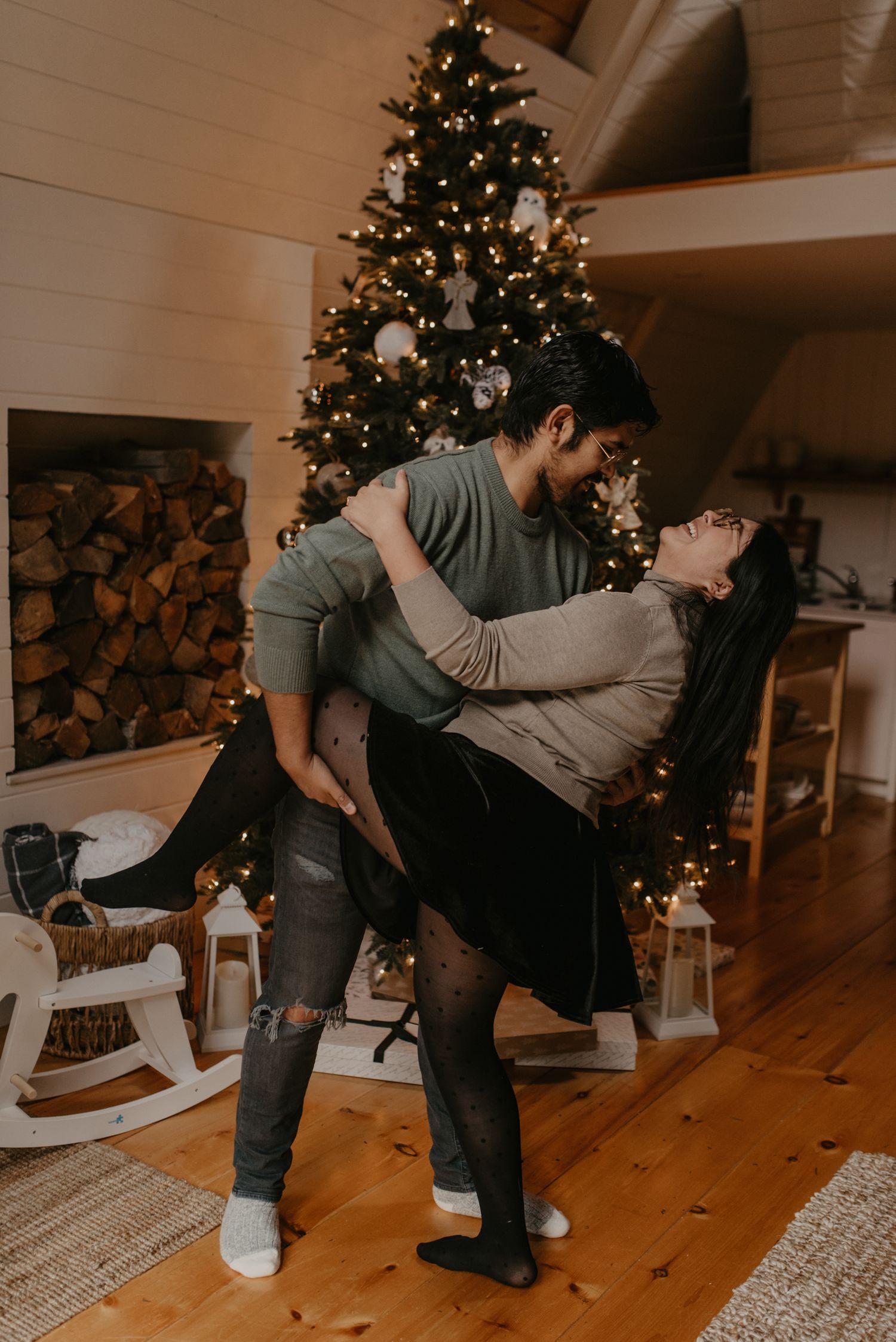 Couple sharing a romantic dance in front of a decorated Christmas tree in a cozy cabin home.