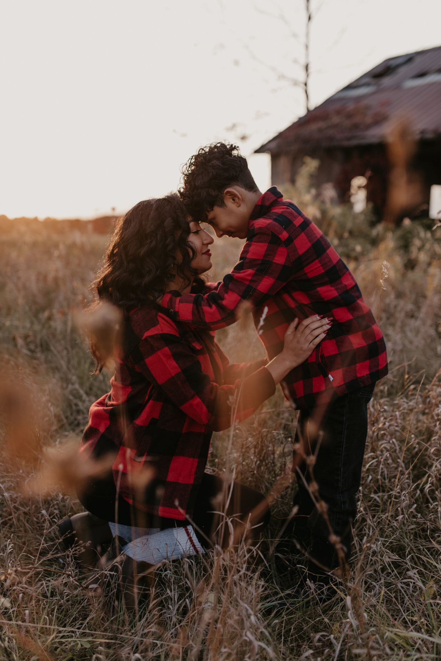 Couple in matching red plaid shirts share romantic moment in golden field at sunset.