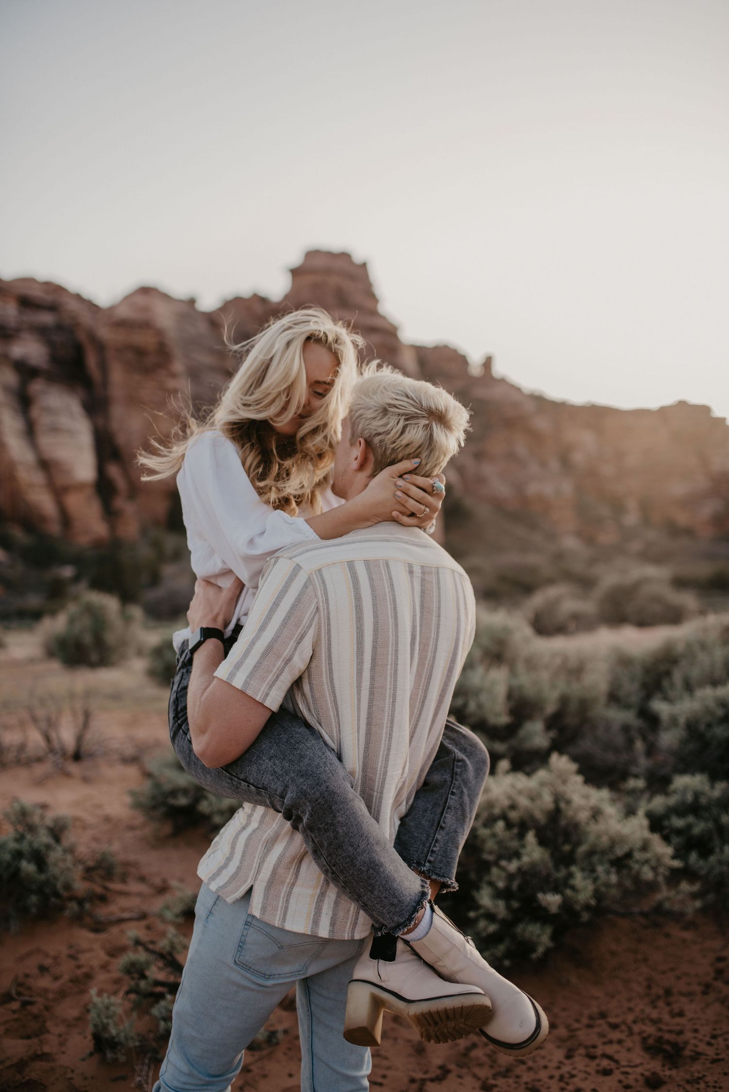 Man lifting woman in a joyful embrace in a scenic red rock desert landscape at sunset.