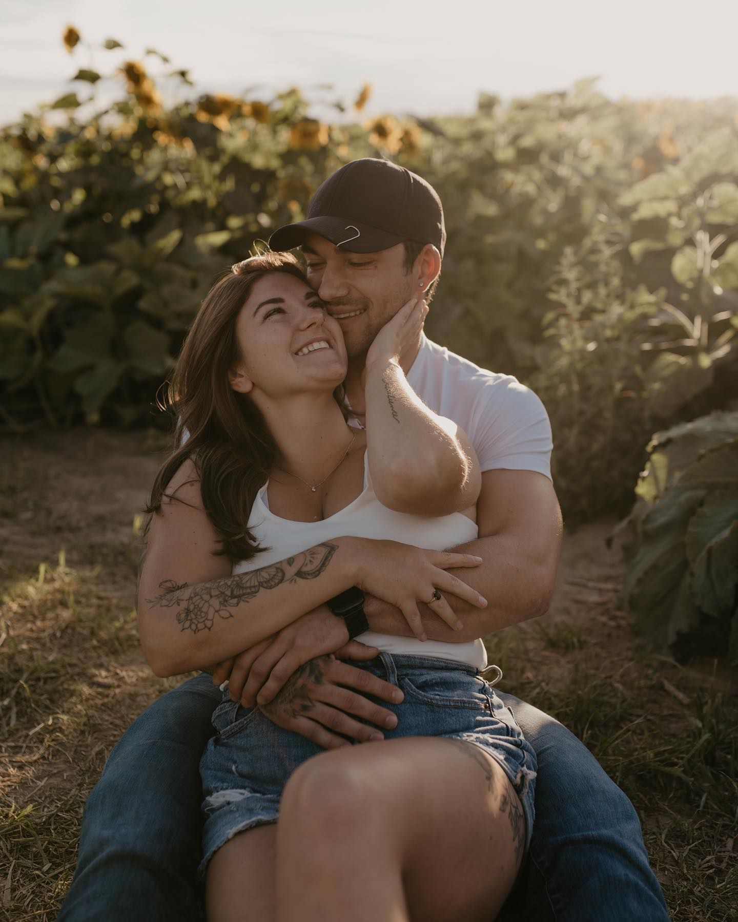 Happy couple embracing and laughing together in a sunflower field during golden hour photo session.