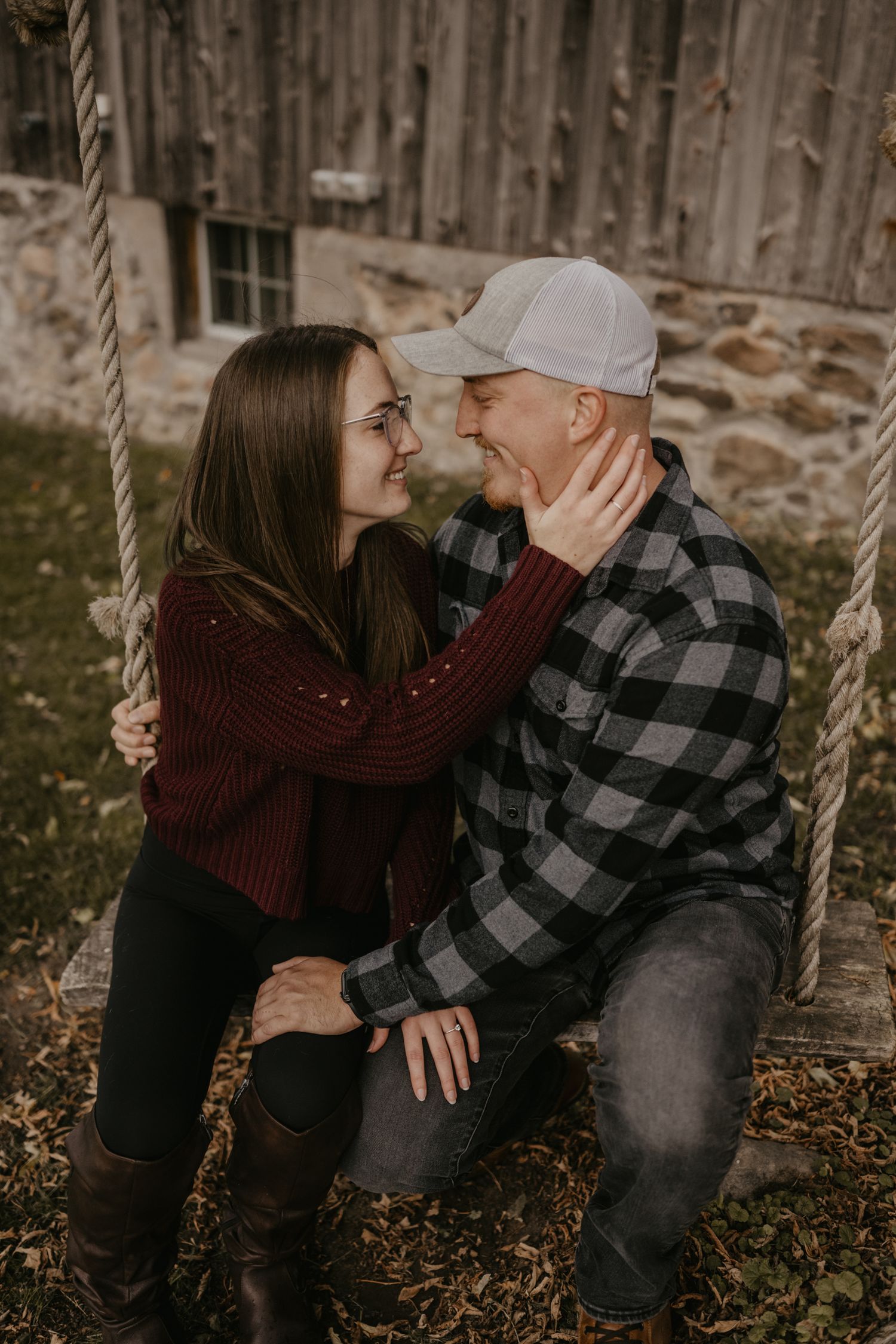 Couple sharing a romantic moment on a rope swing near a rustic stone barn in autumn.