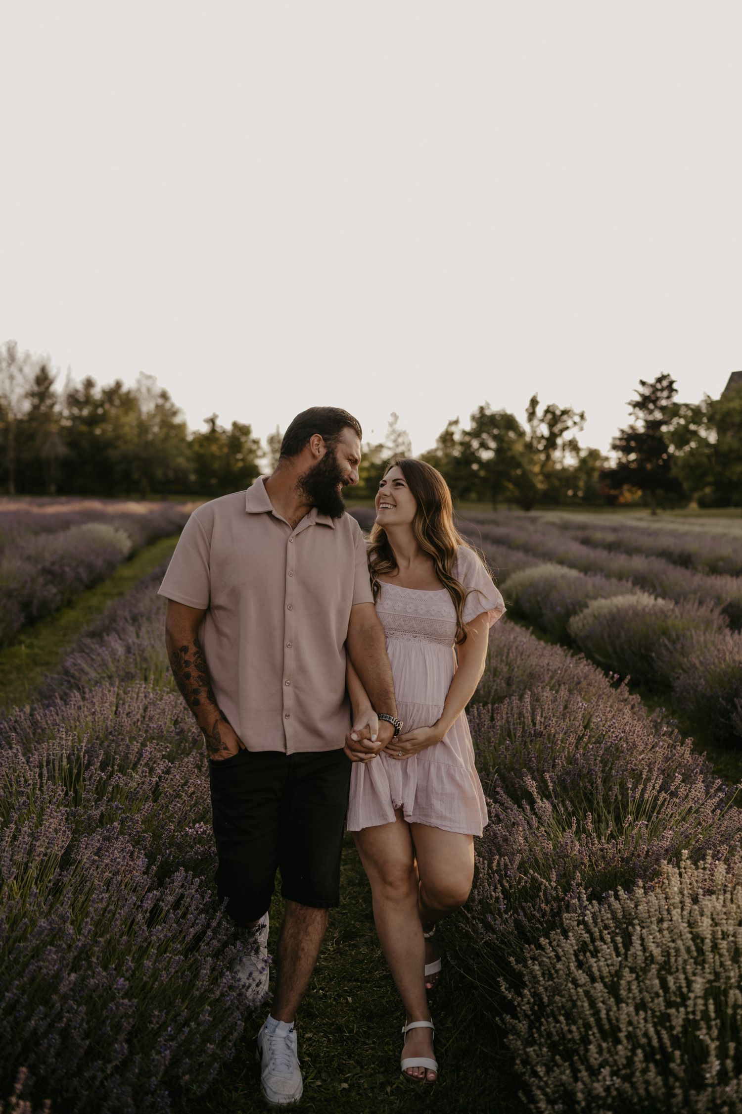 Happy couple holding hands and walking through blooming lavender field at sunset, smiling at each other.
