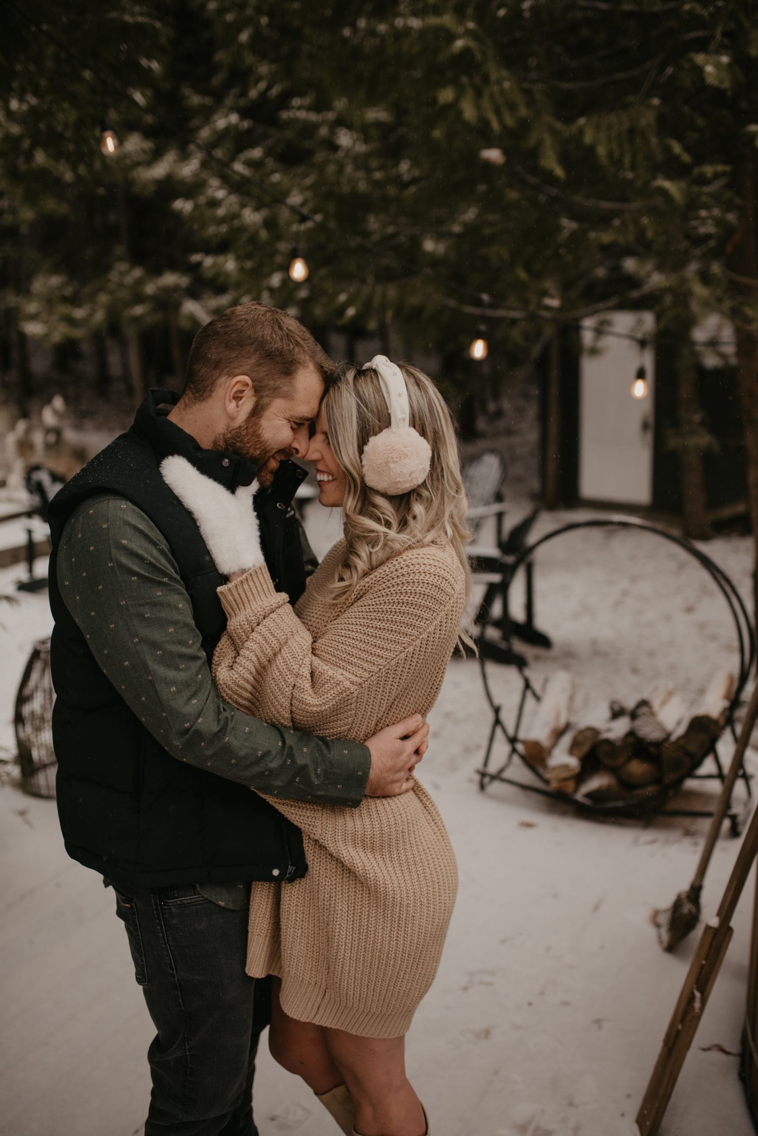 Couple sharing intimate moment in snowy winter setting, woman wearing ear muffs and cozy knit dress.