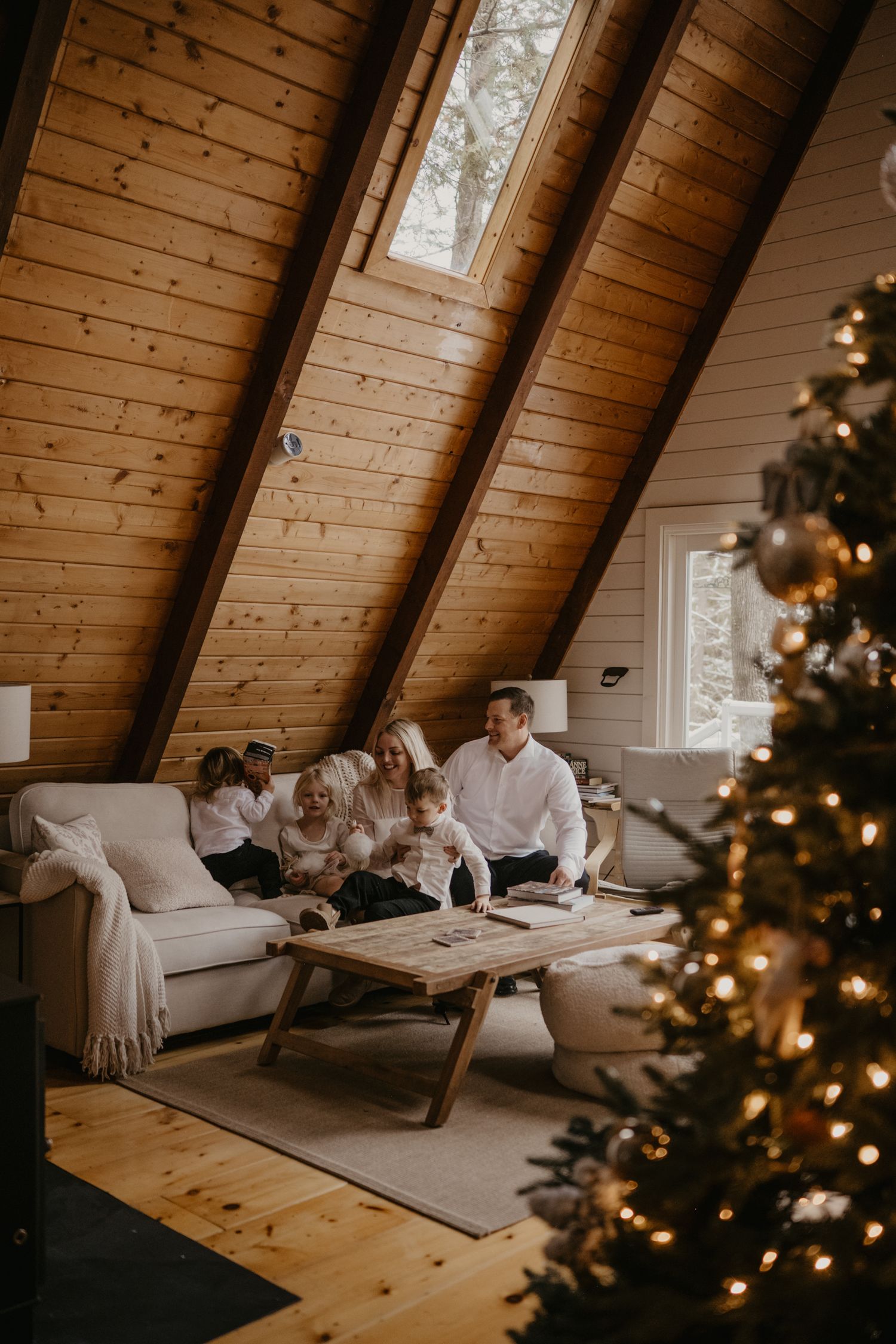 Family relaxing together on a sofa in a warm A-frame cabin with a decorated Christmas tree.