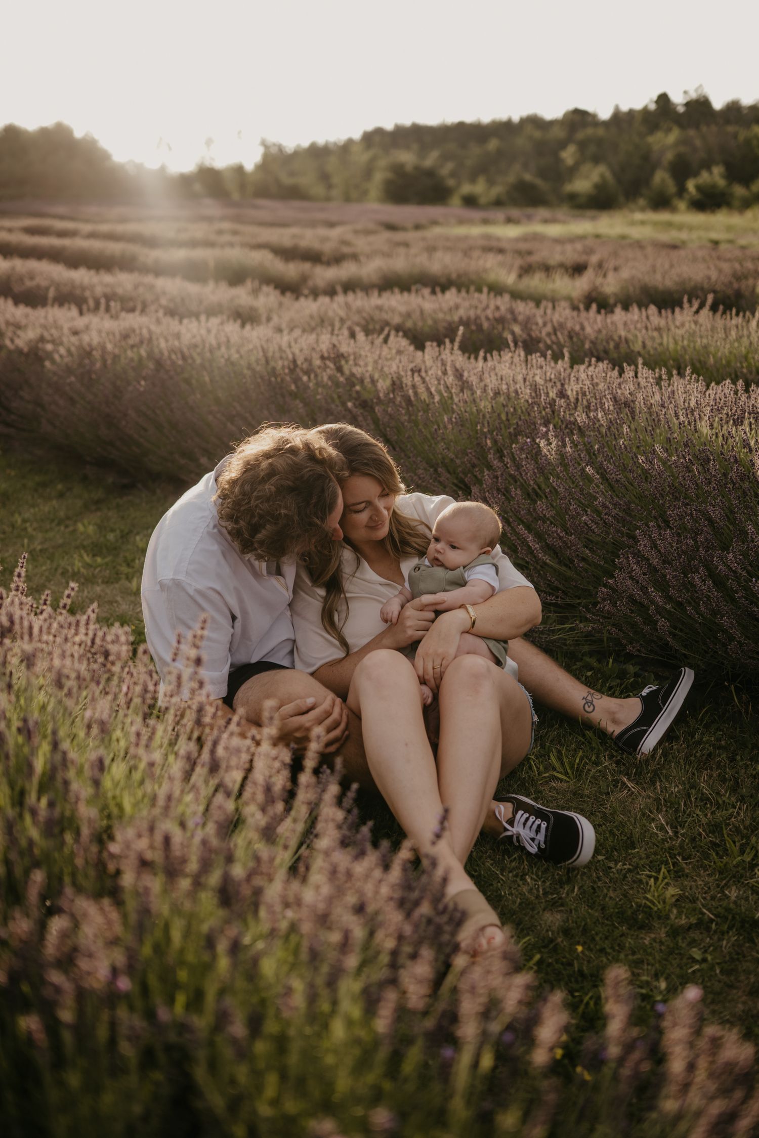 Young couple sitting together in lavender field at sunset, lovingly holding their baby.