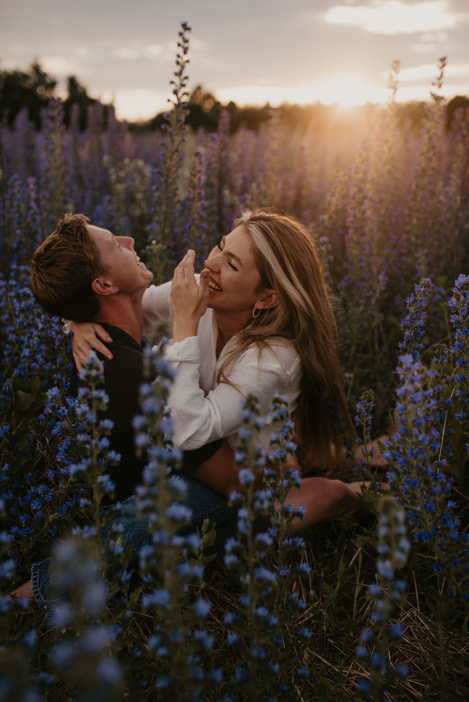 Romantic couple embracing in a field of purple wildflowers during a stunning sunset.