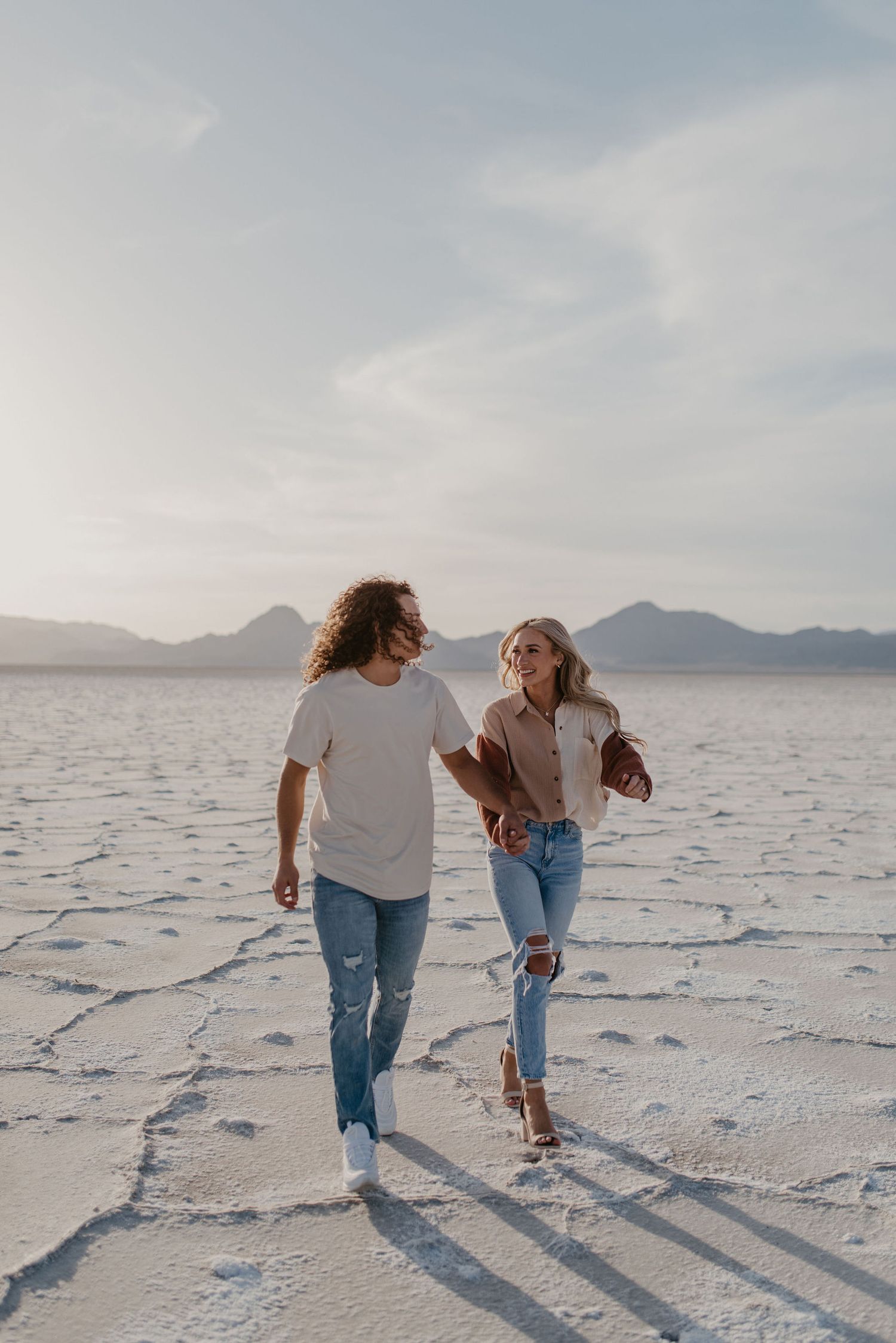 Couple holding hands walking across the Bonneville Salt Flats with mountains in the background.