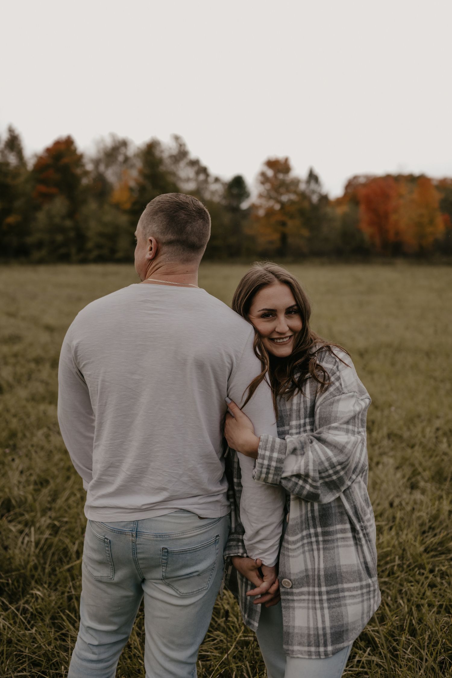 Woman smiles back at camera while holding hands with man in autumn field.