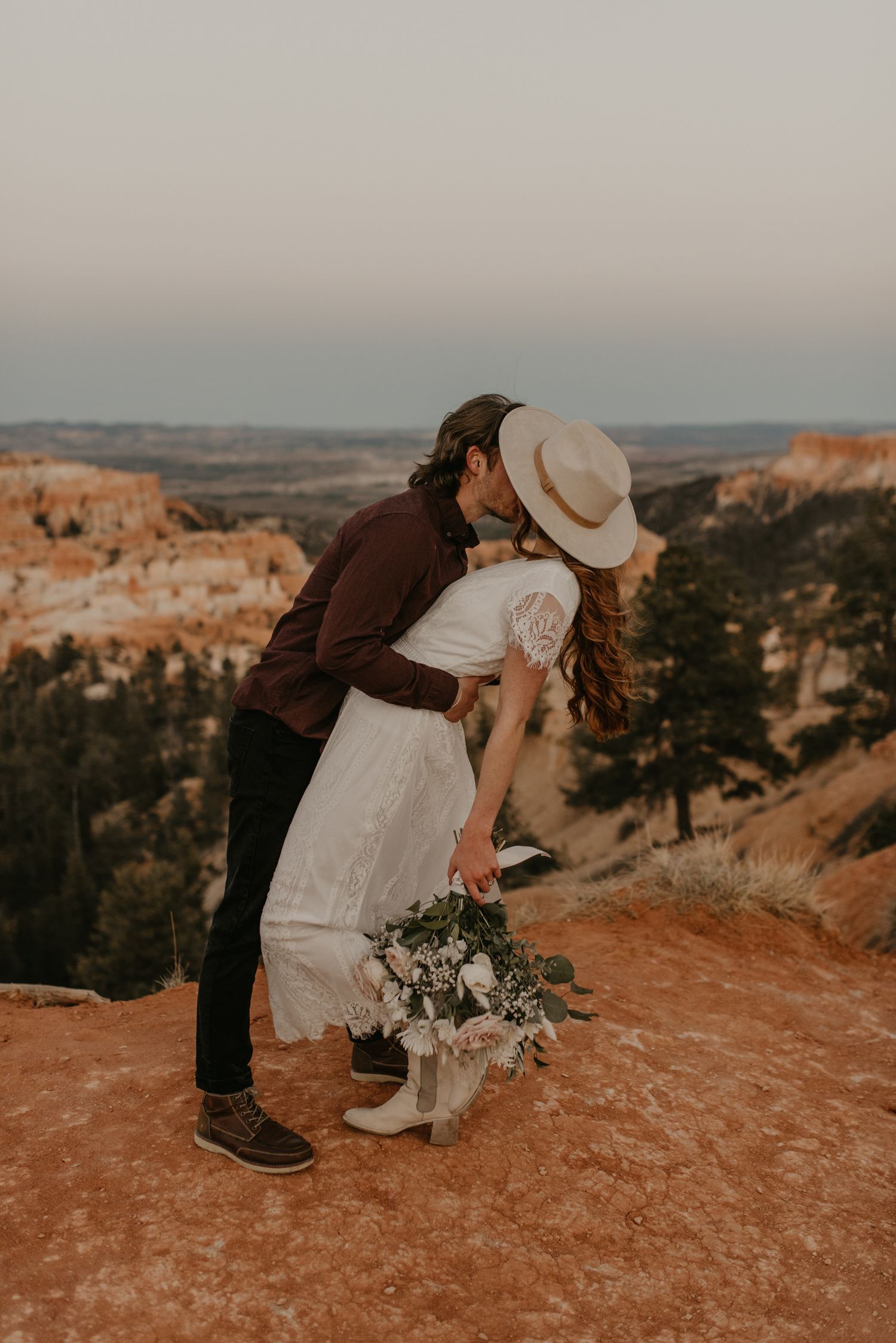 Couple sharing a kiss at Bryce Canyon overlook, bride holding a floral bouquet.