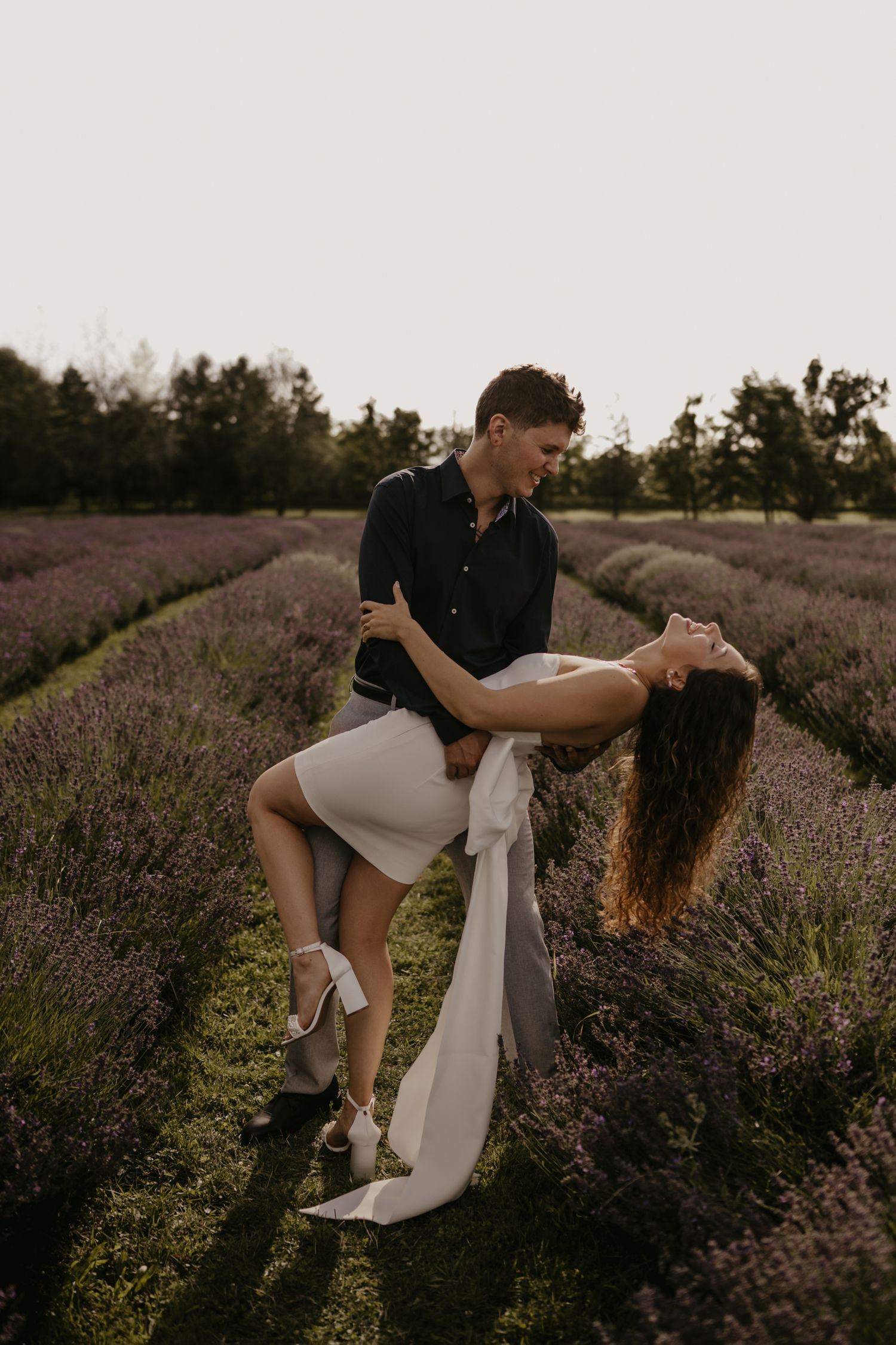 Couple dancing in a lavender field at sunset, man dipping woman in a white mini dress.