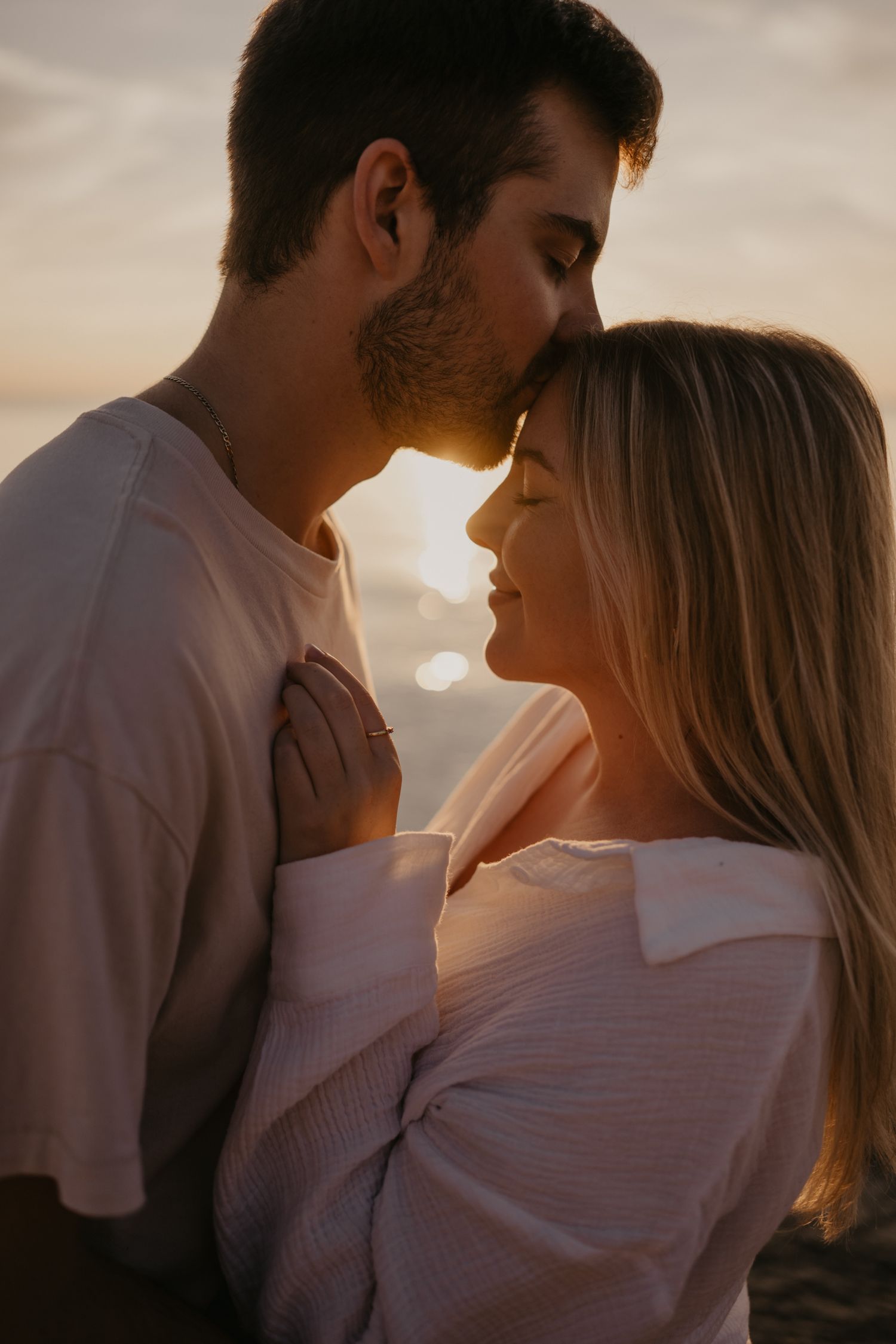 Romantic couple sharing intimate moment at sunset, man kissing woman's forehead on beach.