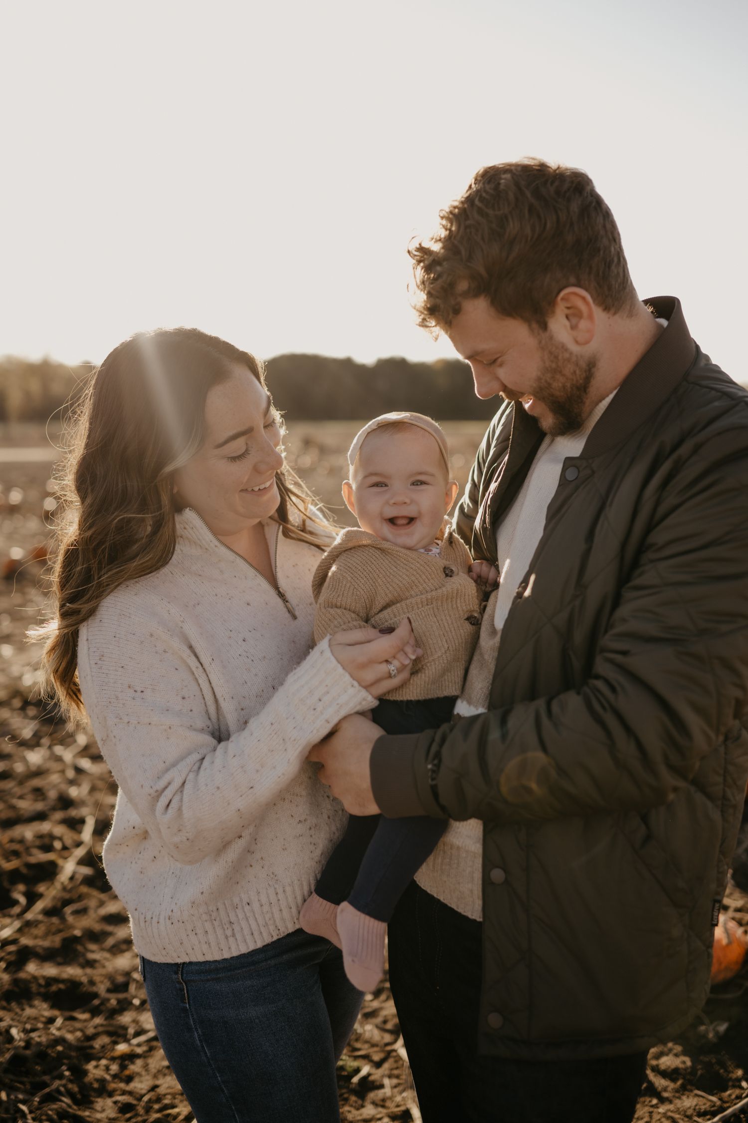 A happy young family with a smiling baby enjoys a sunny autumn day outdoors in a pumpkin field.