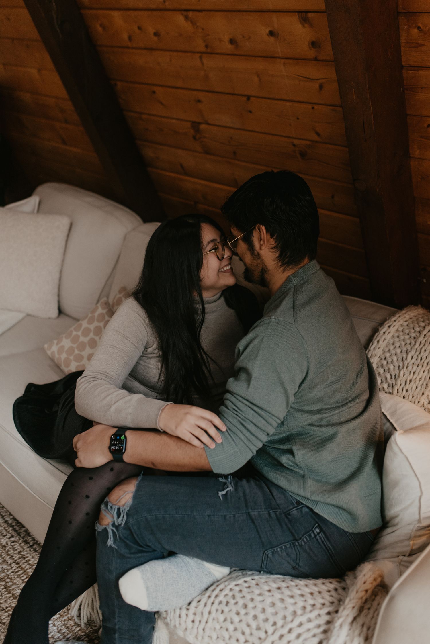 A couple shares a romantic moment cuddling on a cozy white sofa in a rustic wood-paneled cabin loft.