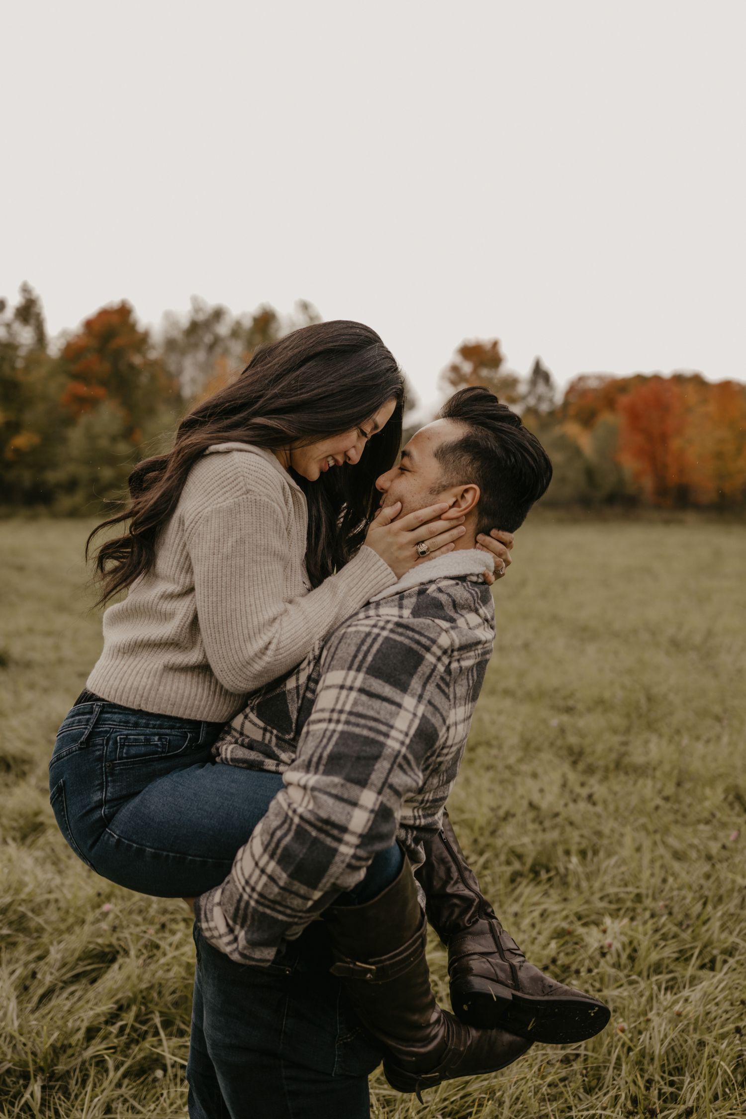 Man lifting woman in romantic embrace in open field with colorful fall foliage.