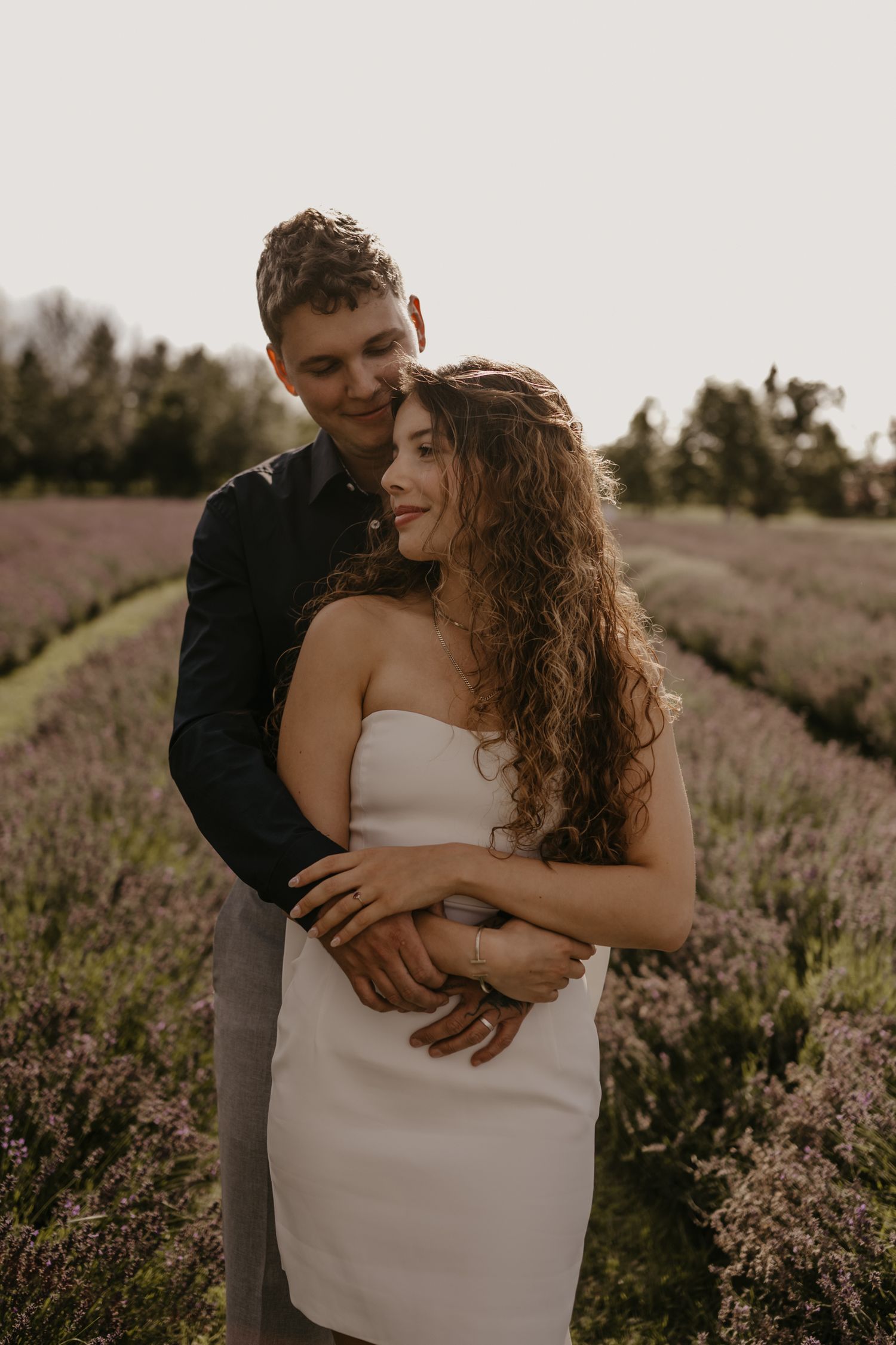 Couple embracing in a blooming lavender field at dusk, woman in white strapless dress.