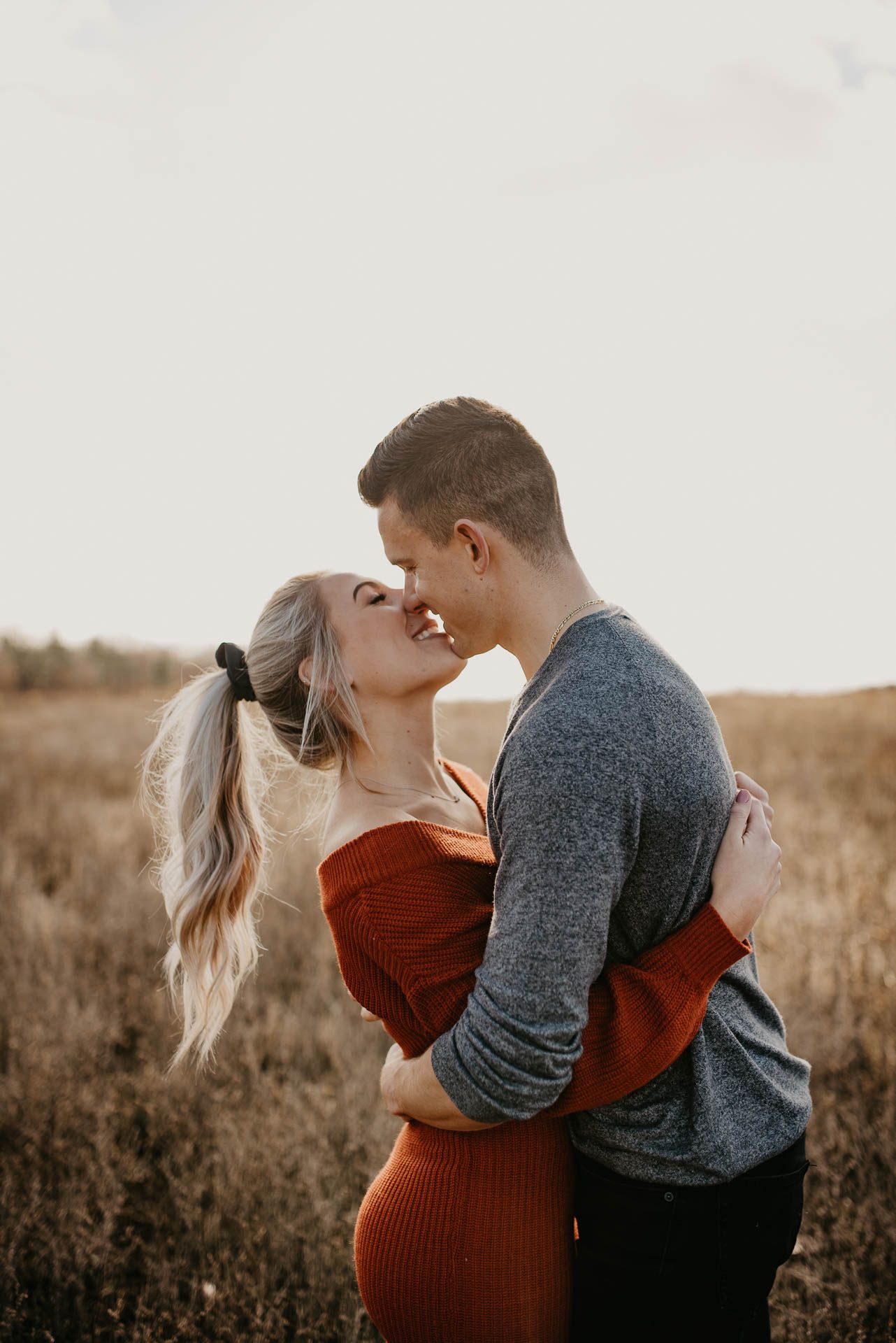 Couple about to kiss while embracing in a golden field during a warm fall outdoor photo session.