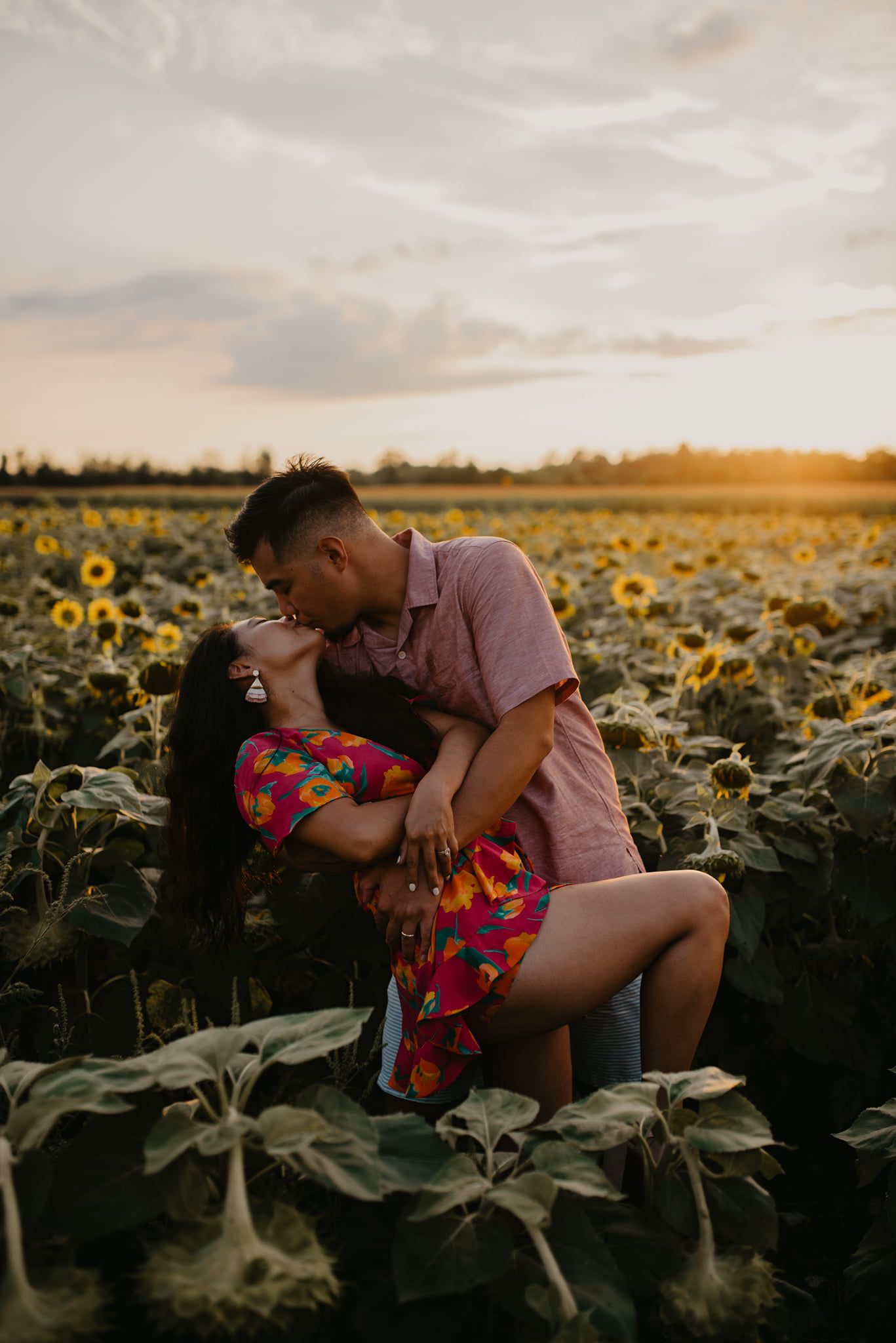 Couple sharing a romantic dip kiss in a sunflower field during a stunning golden hour sunset.