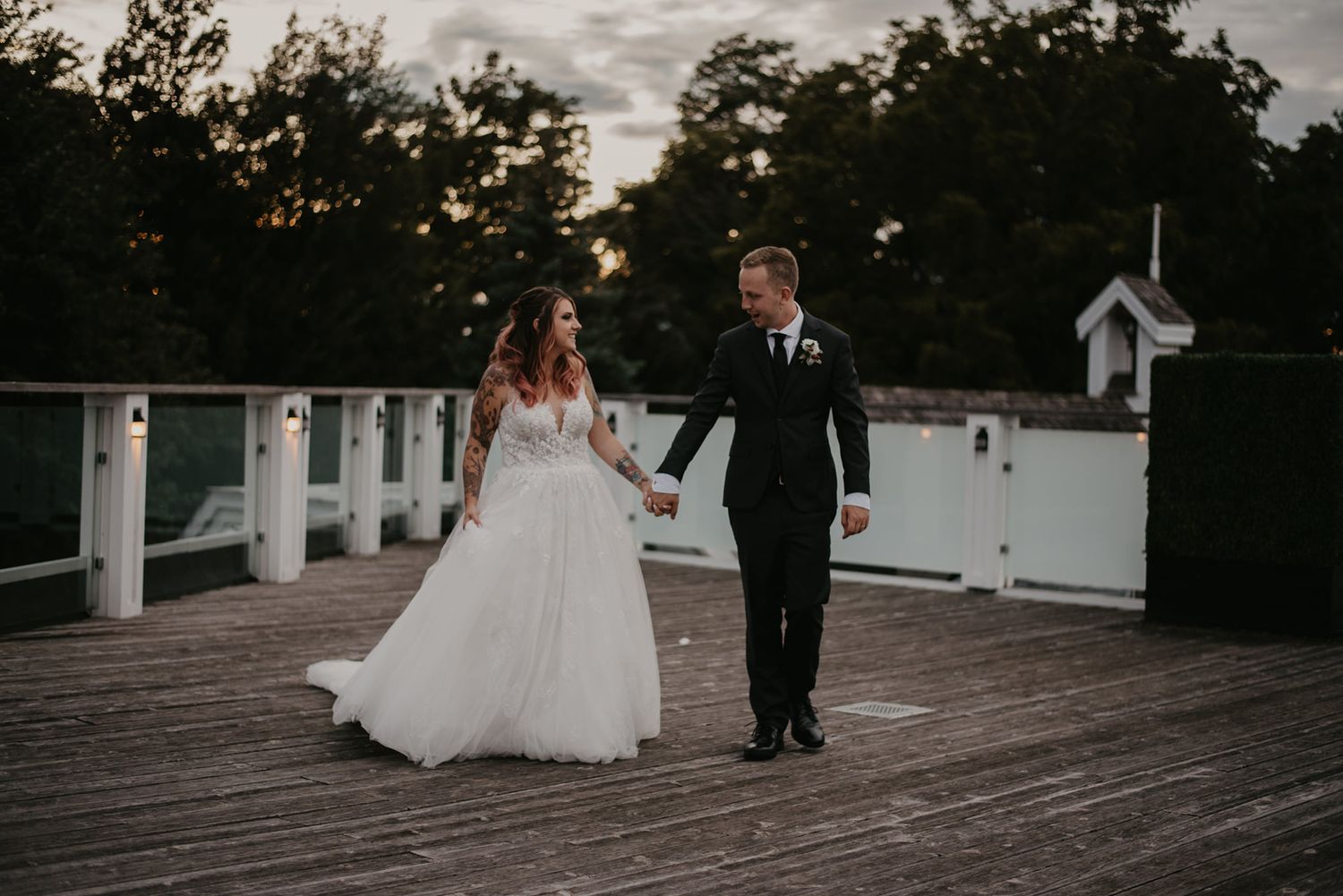Bride and groom walking hand in hand on a wooden dock at dusk after wedding ceremony.