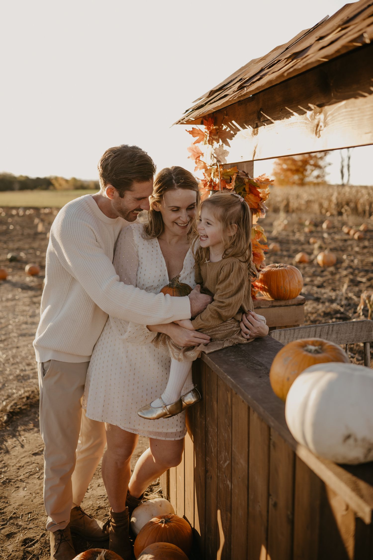 A happy family of three enjoys a sunny autumn day at a pumpkin patch, surrounded by fall foliage and pumpkins.